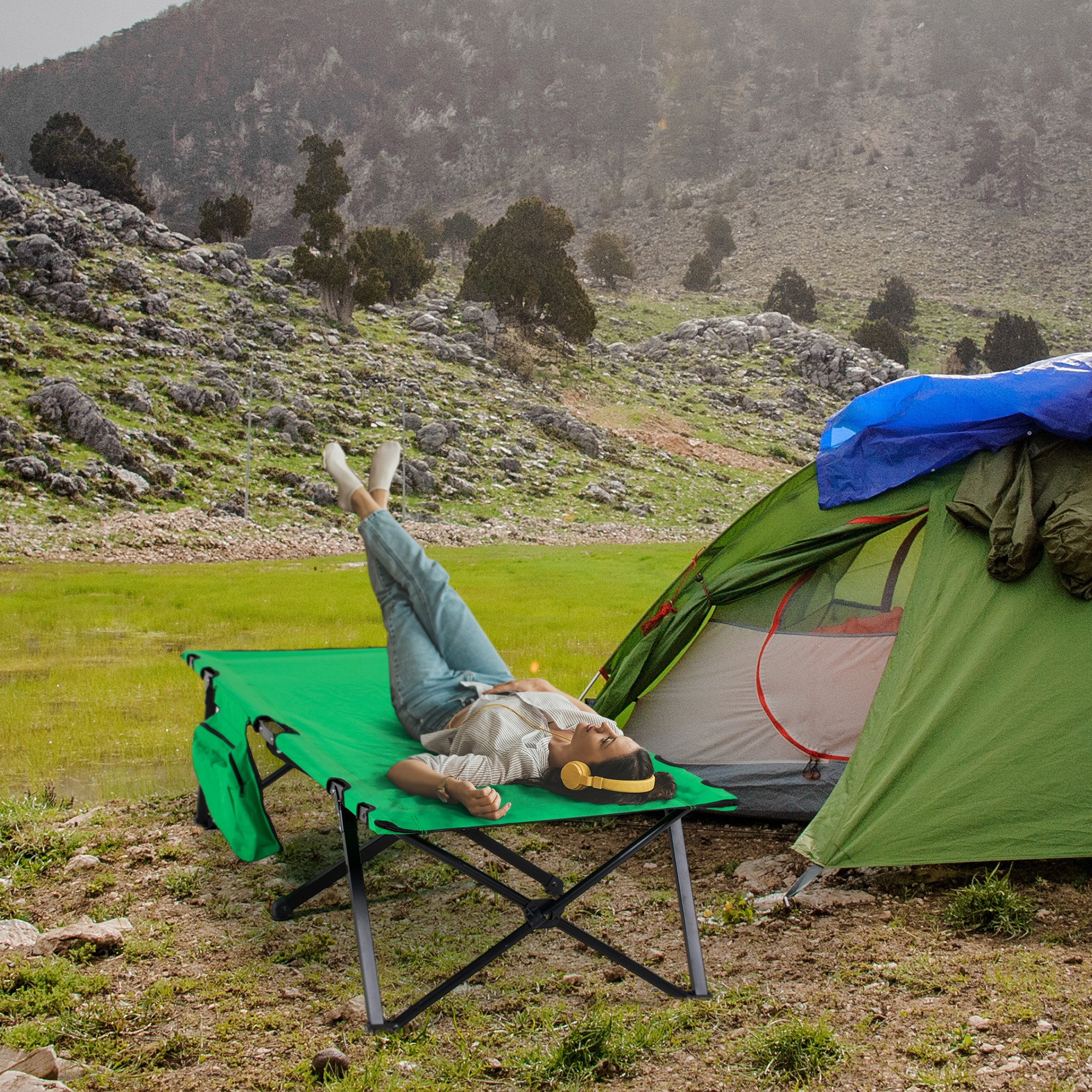 Eine Person liegt mit Kopfhörern auf einem grünen Campingbett im Freien.