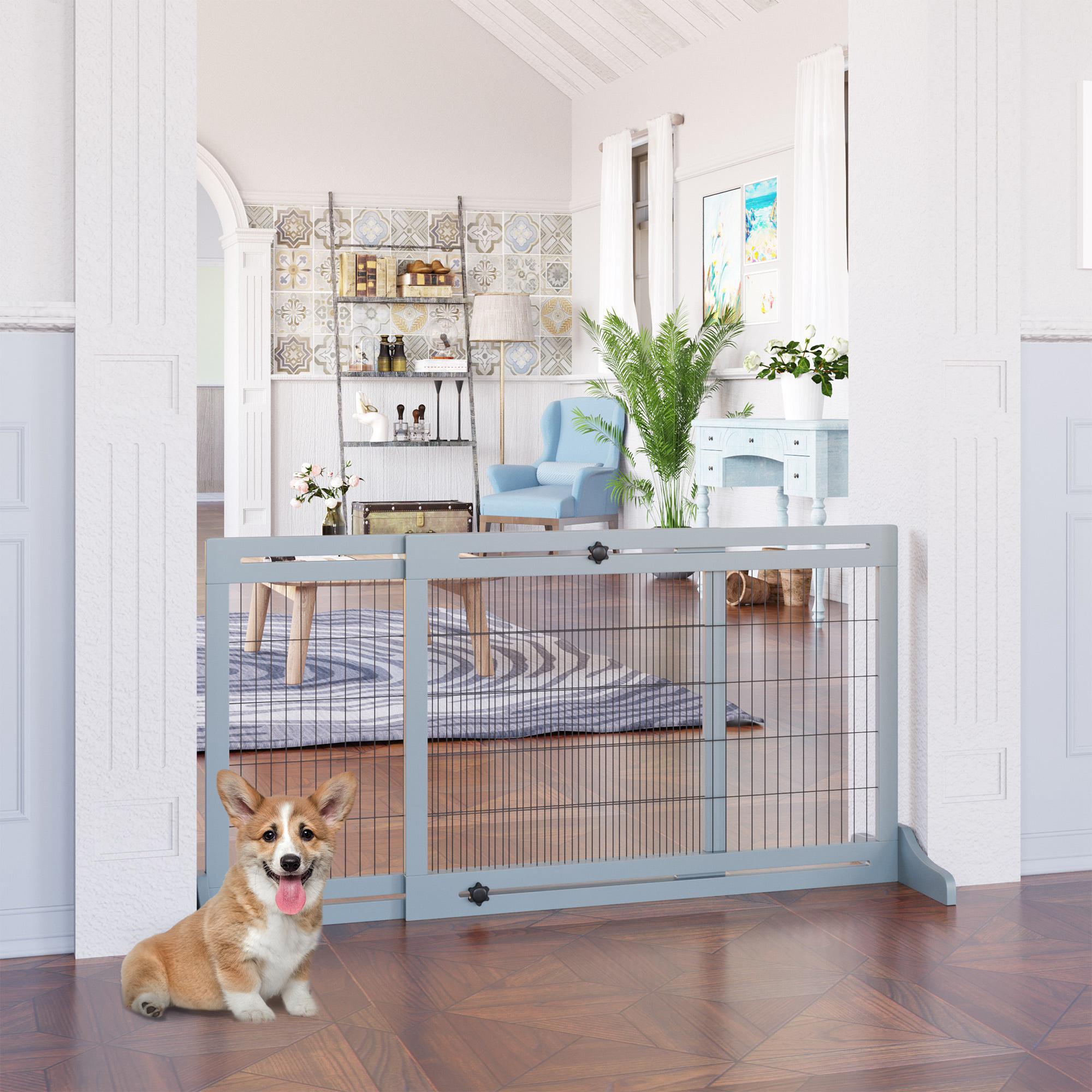 Ein Corgi sitzt neben einem grauen Haustiergitter. Das Gitter befindet sich in einem hellen Raum mit Fenster.