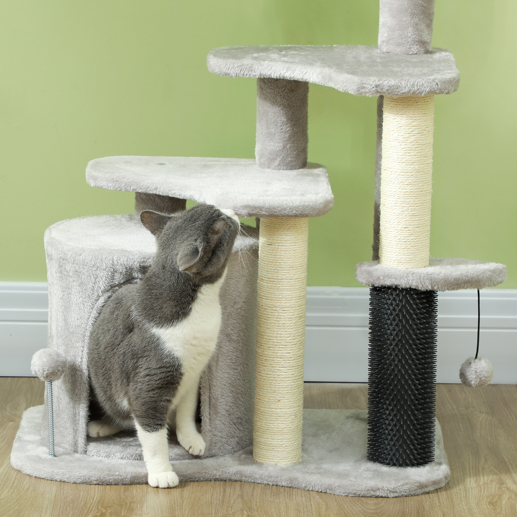 Eine grau-weiße Katze, die auf einen mehrstöckigen grauen Katzenbaum blickt. Grüner Wandhintergrund.