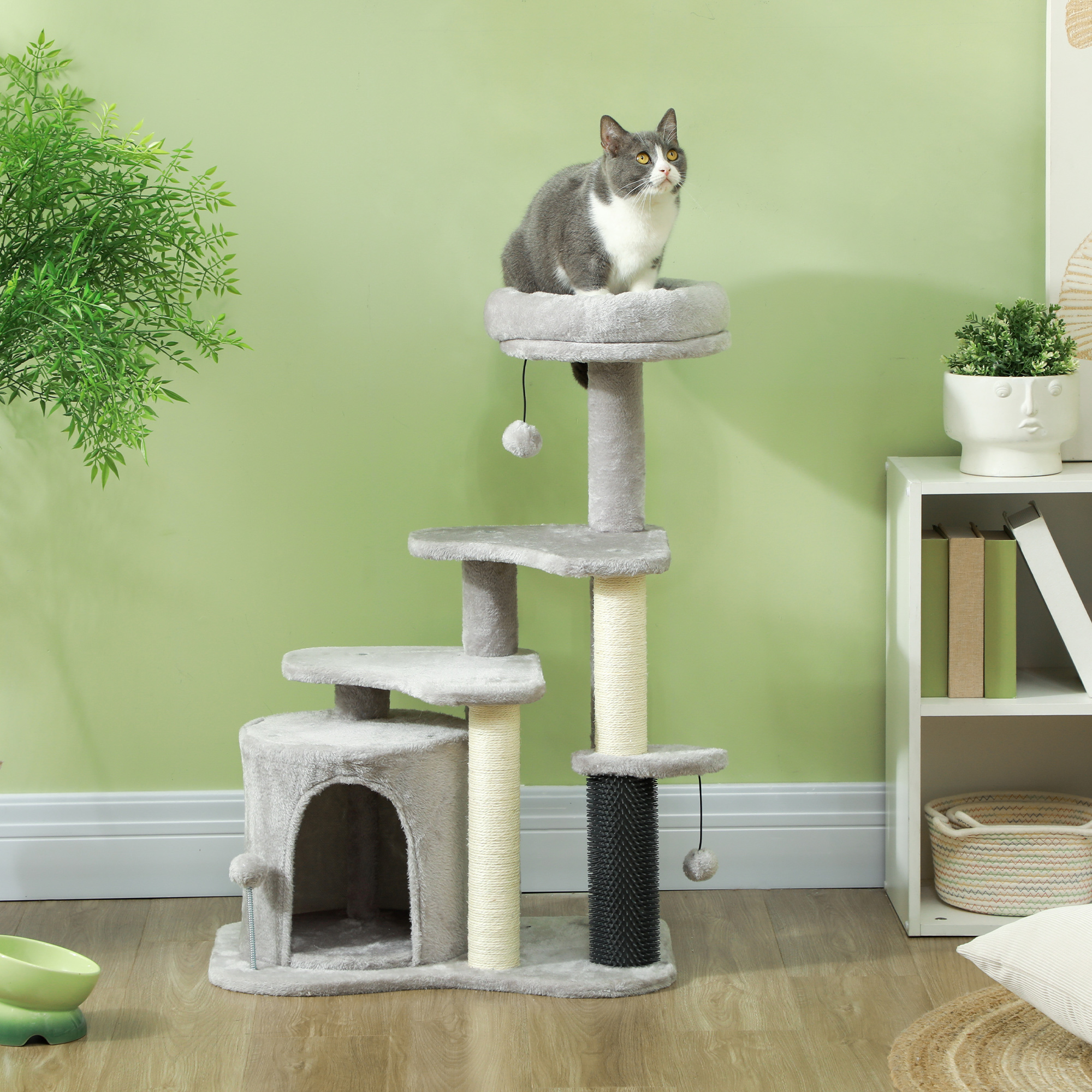 Eine grau-weiße Katze auf einem mehrstöckigen Katzenbaum. Grüner Wand- und weißer Schrankhintergrund.