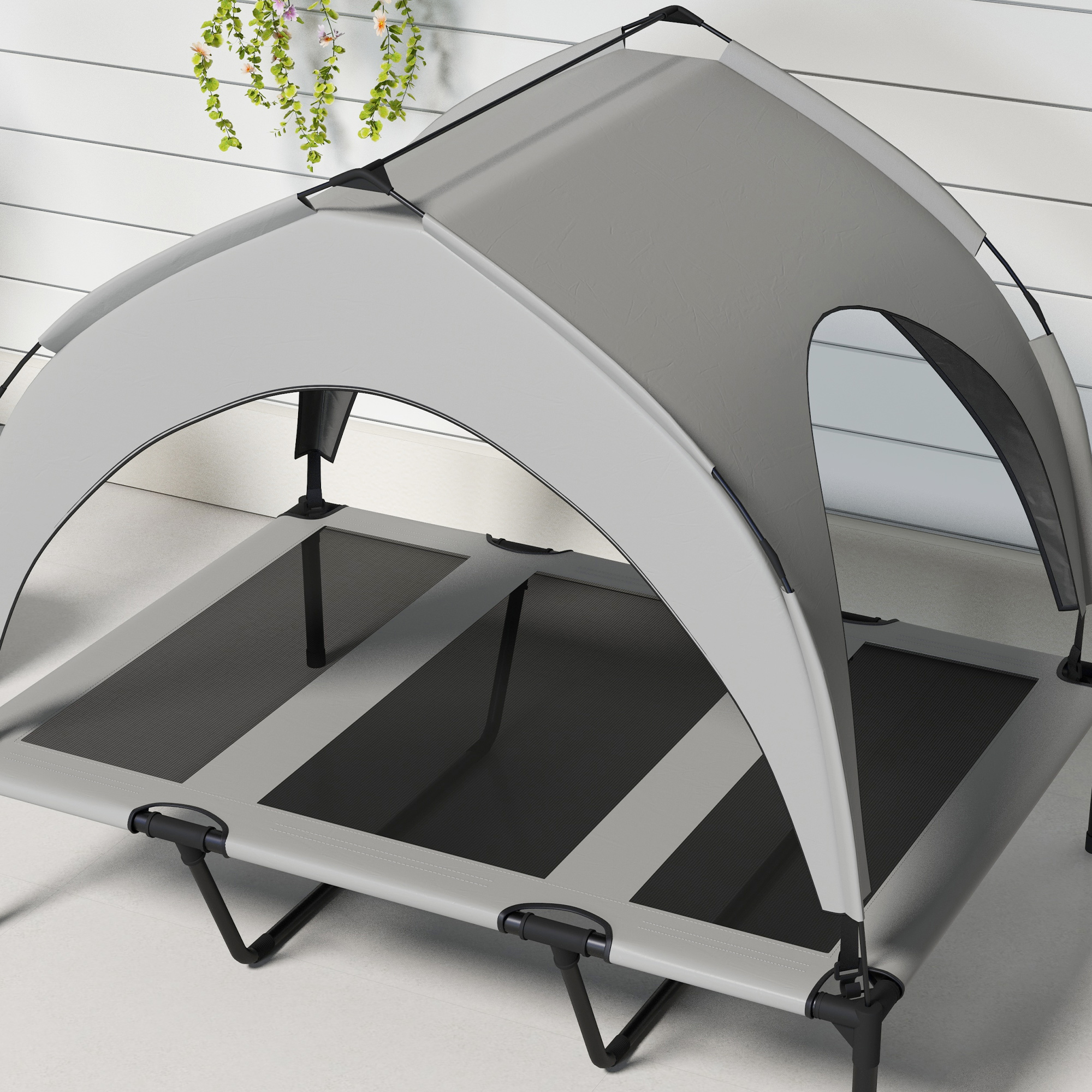 Cama para perros con dosel, gris y negro. Plantas y pared blanca en el fondo.