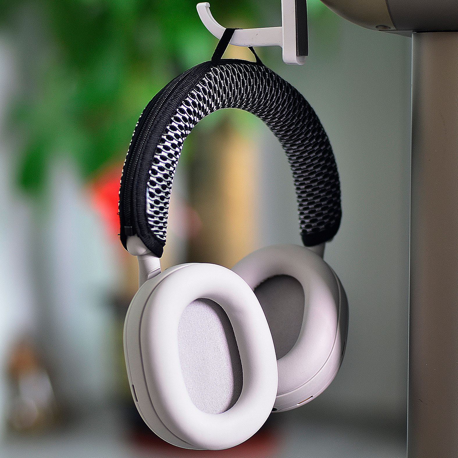 Weiße Kopfhörer mit schwarzem Mesh oben, hängen an einem Haken. Der Hintergrund ist unscharf.
