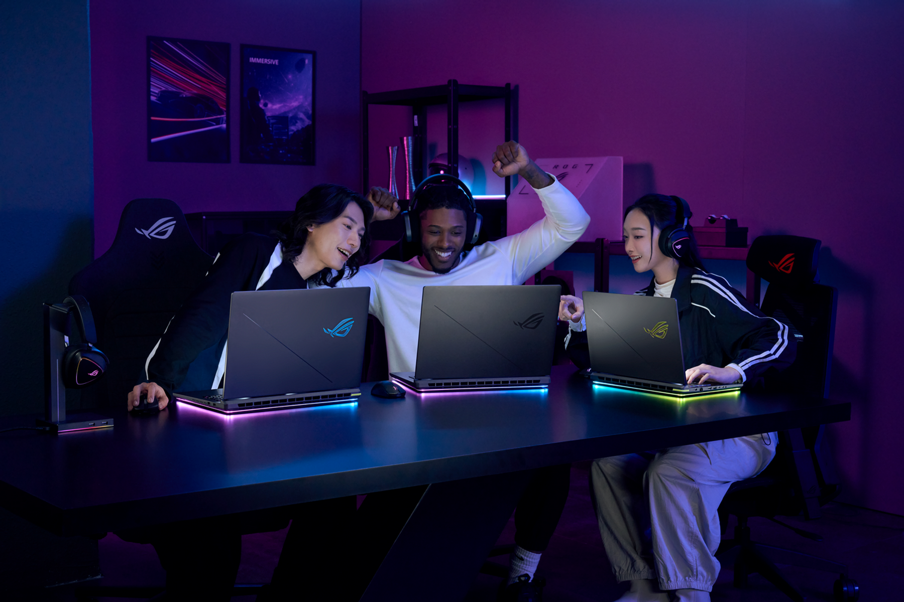 Tres personas juegan con portátiles. Se sientan alrededor de una mesa con luces coloridas, en una habitación oscura.