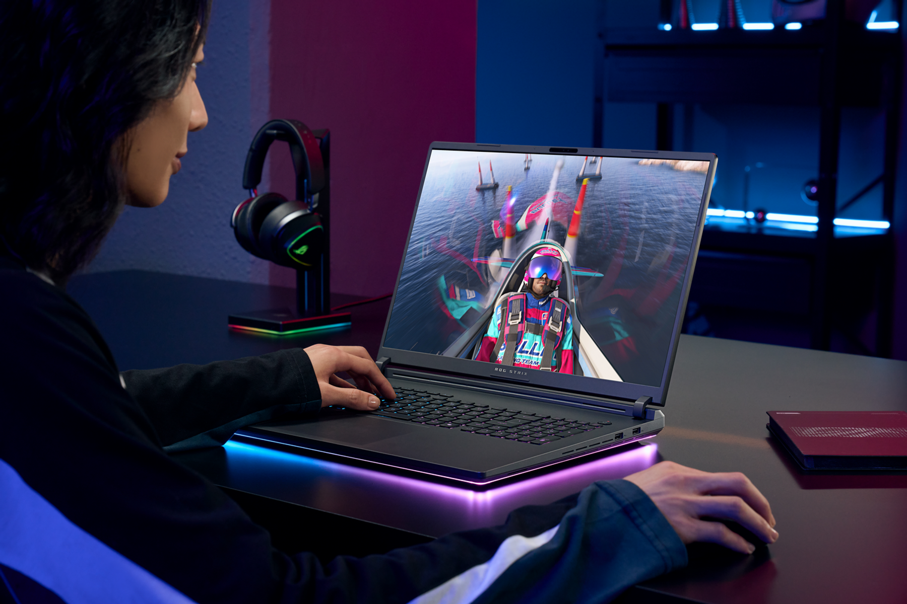Un jugador usa una laptop, jugando un juego de carreras, con auriculares y una lámpara de escritorio.