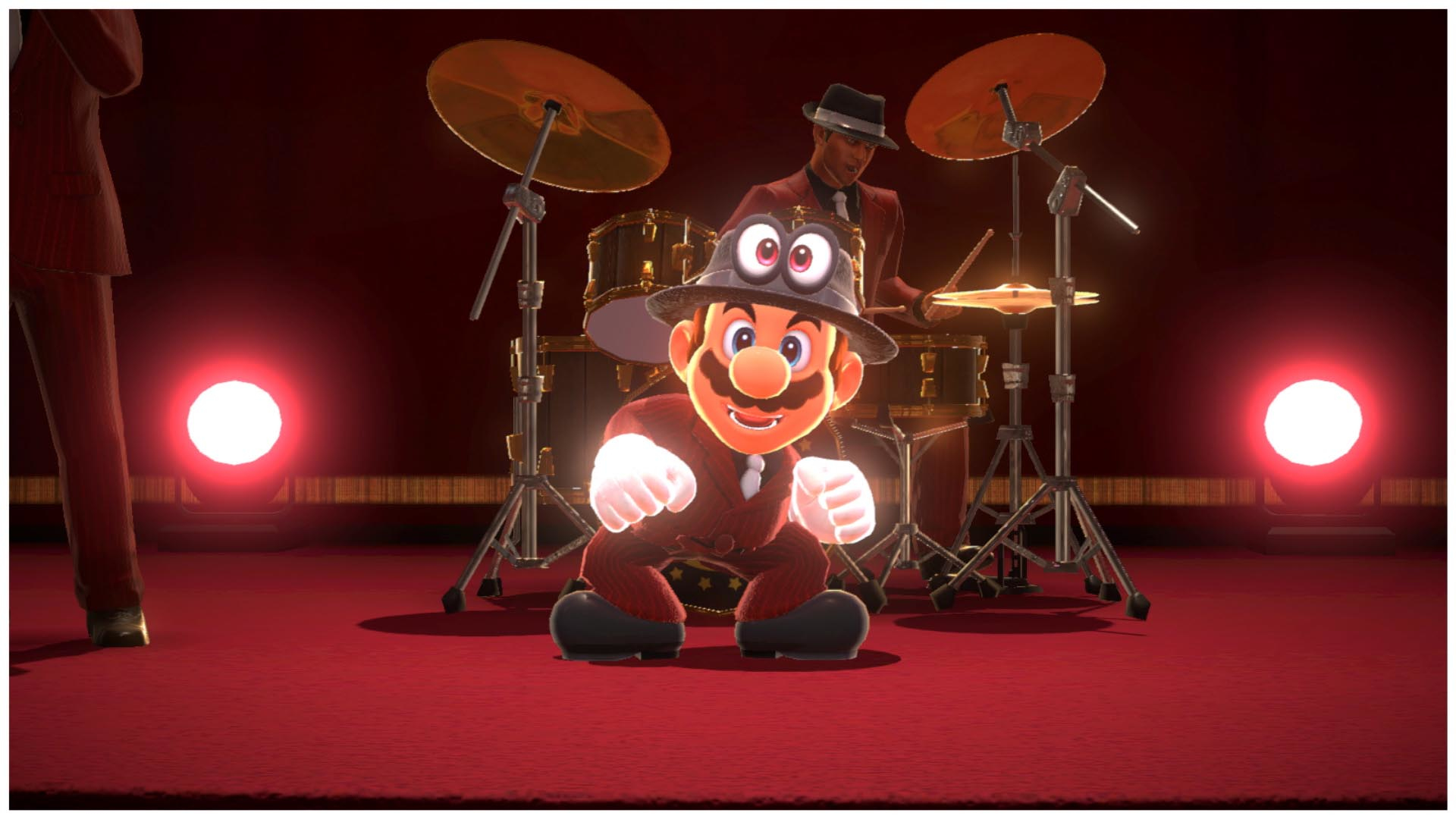 Mario in abito con cappello e occhiali da sole posa davanti a una band su un palco rosso.