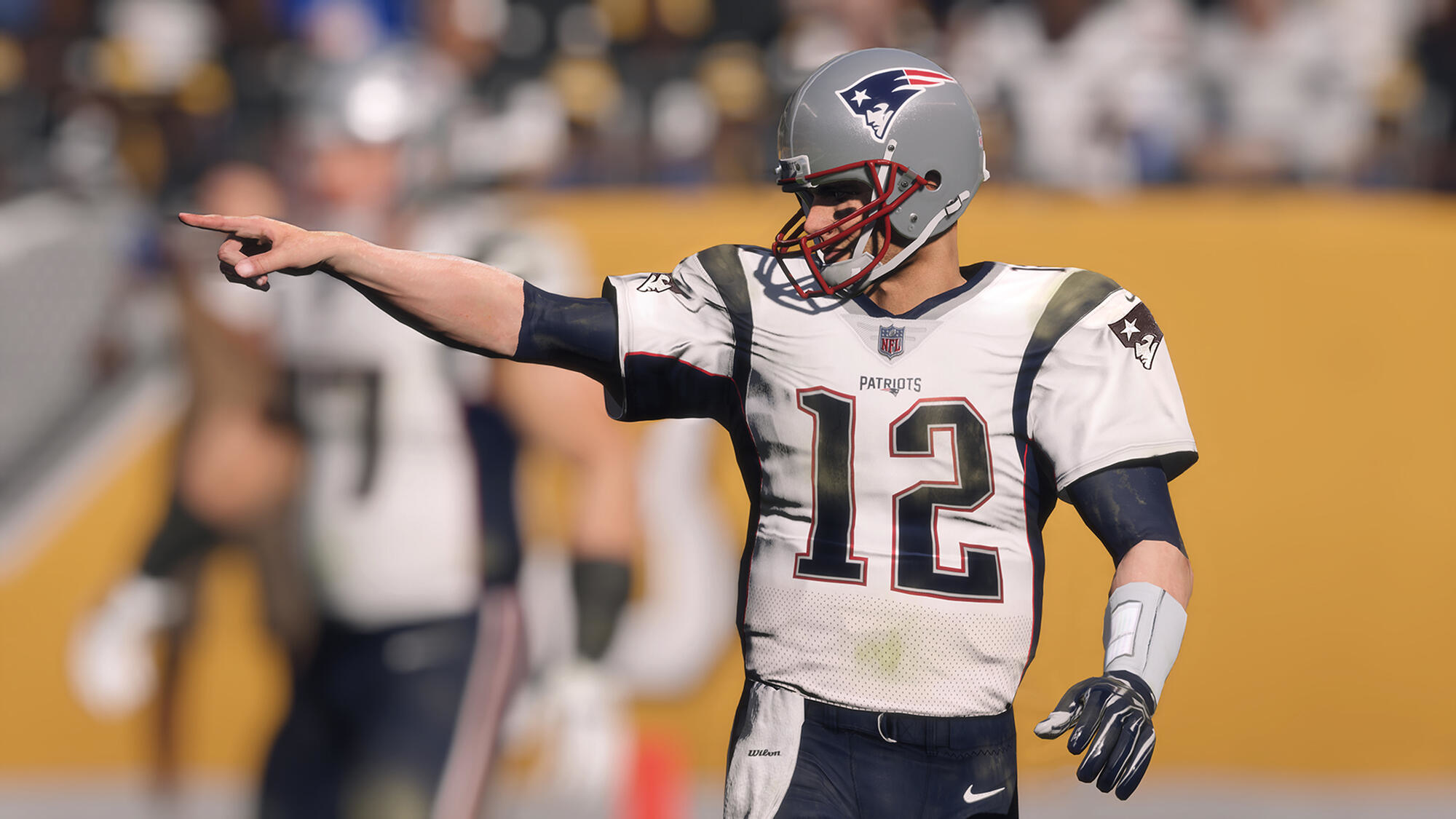 Giocatore di football che indica, indossa una maglia bianca dei Patriots con il numero 12. Stadio.