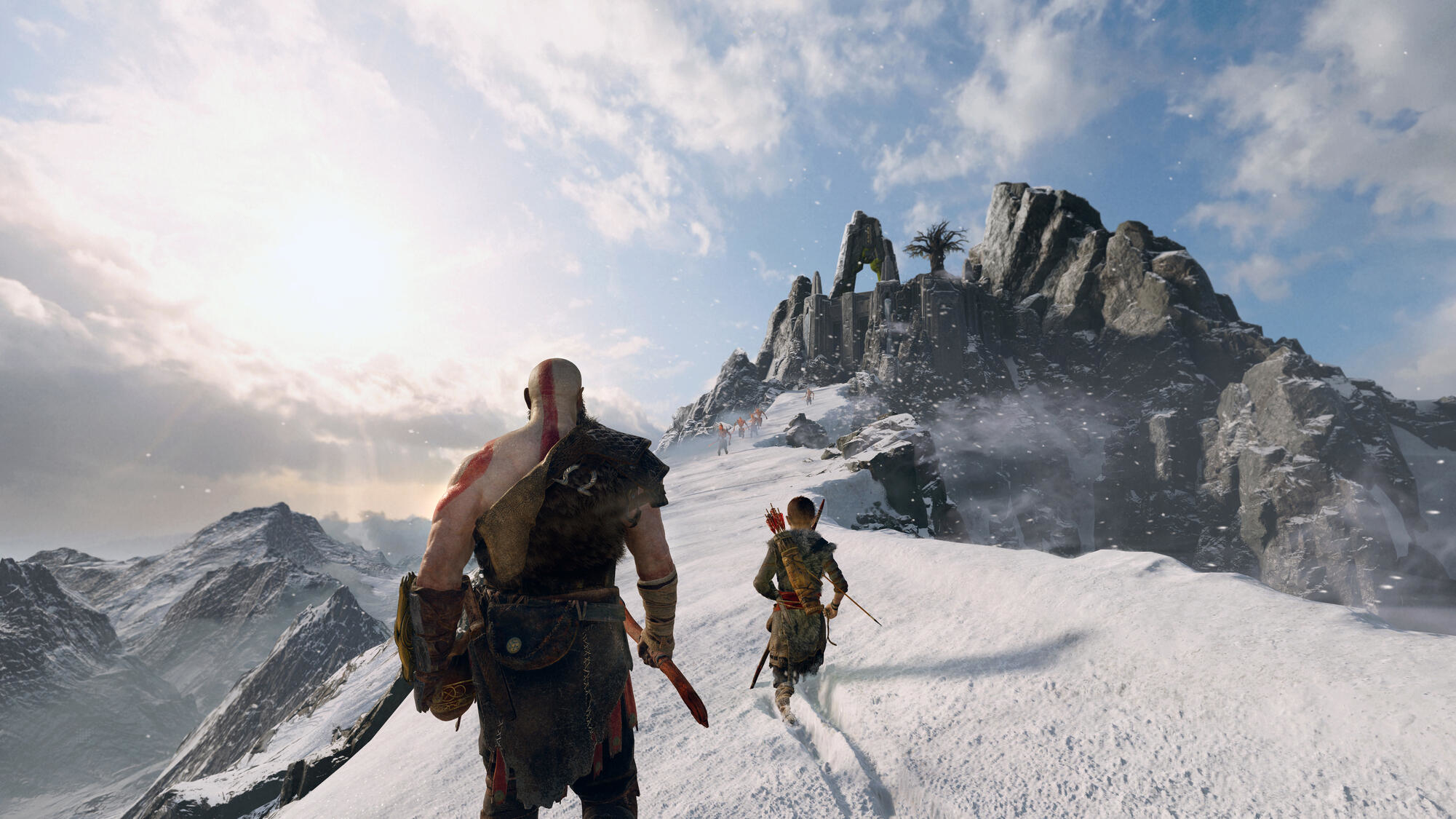 Kratos i Atreus wędrują po ośnieżonej górze. W tle góry i niebo.