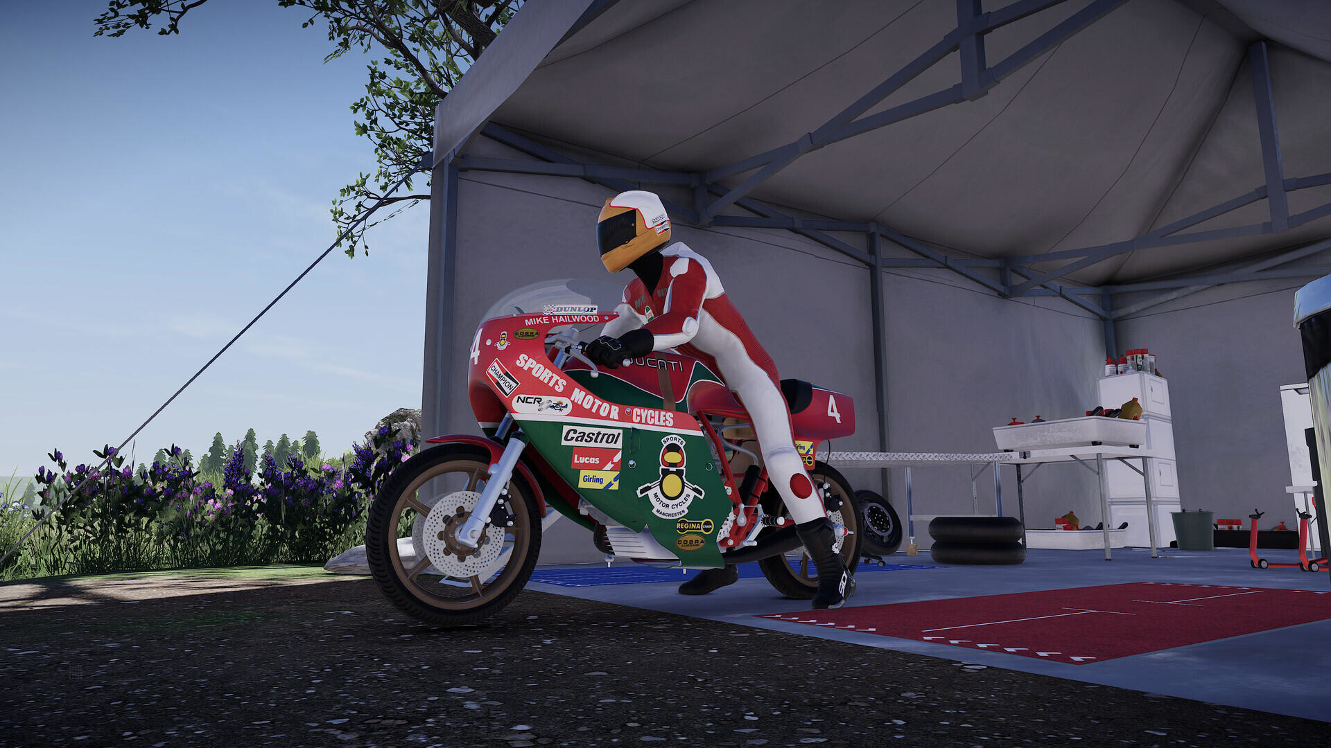 Piloto de moto en una pista. Moto roja y blanca, carpa en la pista y cielo azul al fondo.