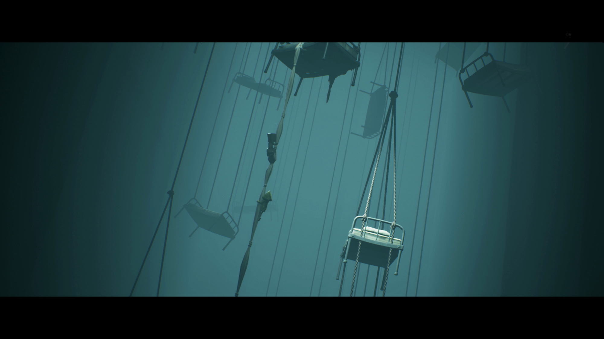 Puste krzesła wiszą na linach w ciemnym, mglistym otoczeniu.