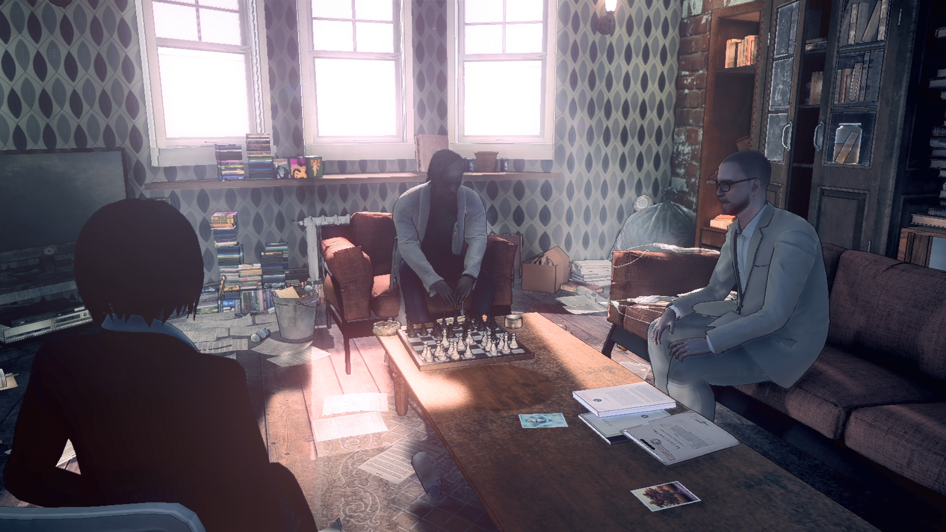 Trzy osoby w pokoju z szachownicą, książkami i dokumentami.