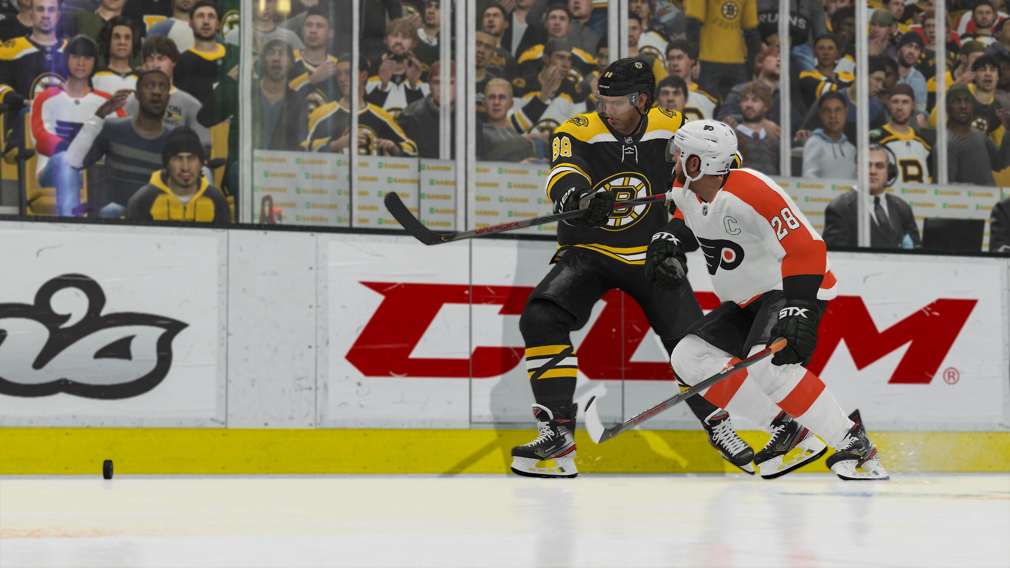 Eishockeyspieler auf dem Eis. Einer in Schwarz und Gelb, der andere in Orange und Weiß, kämpfen um den Puck.