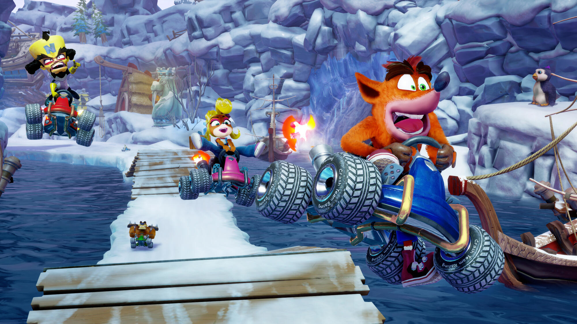 Crash Bandicoot i przyjaciele ścigają się na lodowym torze. Pingwiny i zaśnieżone góry w tle.
