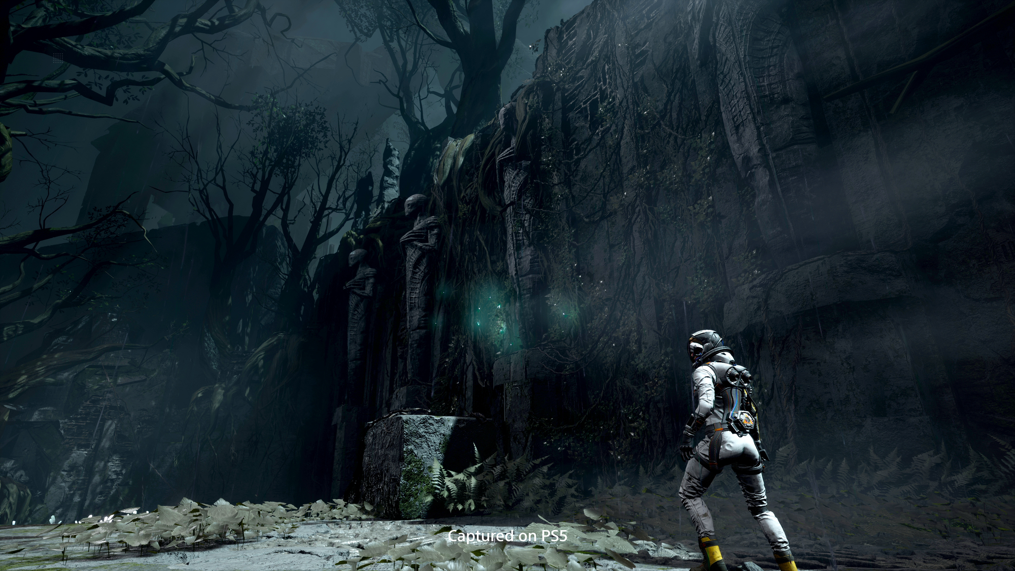 Osoba w białym kombinezonie w ciemnym, zarośniętym otoczeniu. Starożytne posągi w tle.