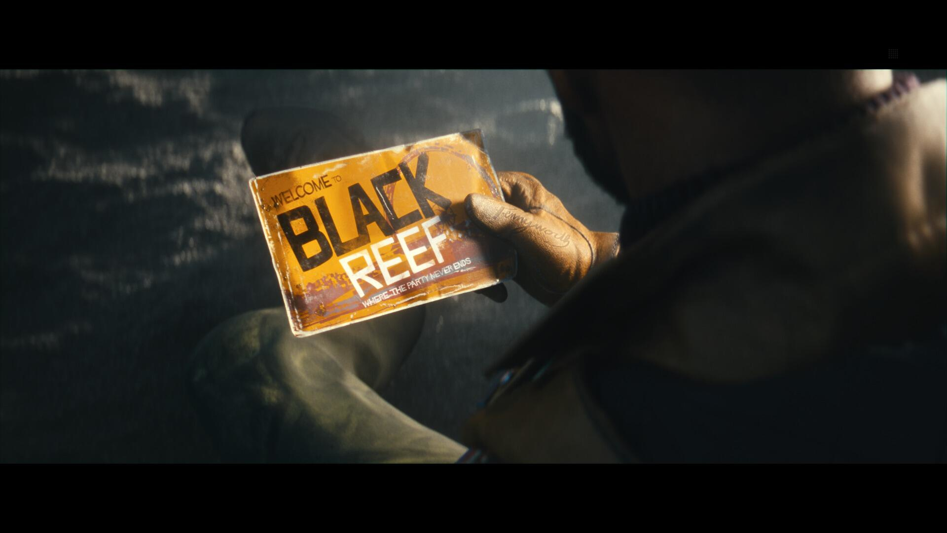 Osoba trzyma kartę z napisem 'Welcome to Black Reef', tytuł gry.