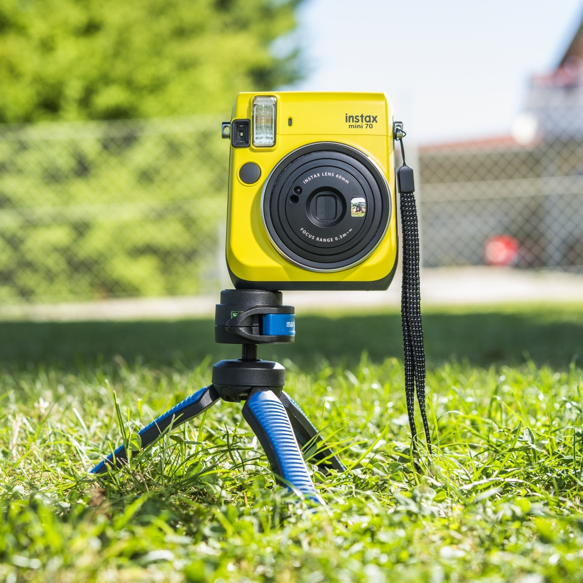 Żółty aparat Instax Mini 70 na statywie, na zielonym trawiastym polu.