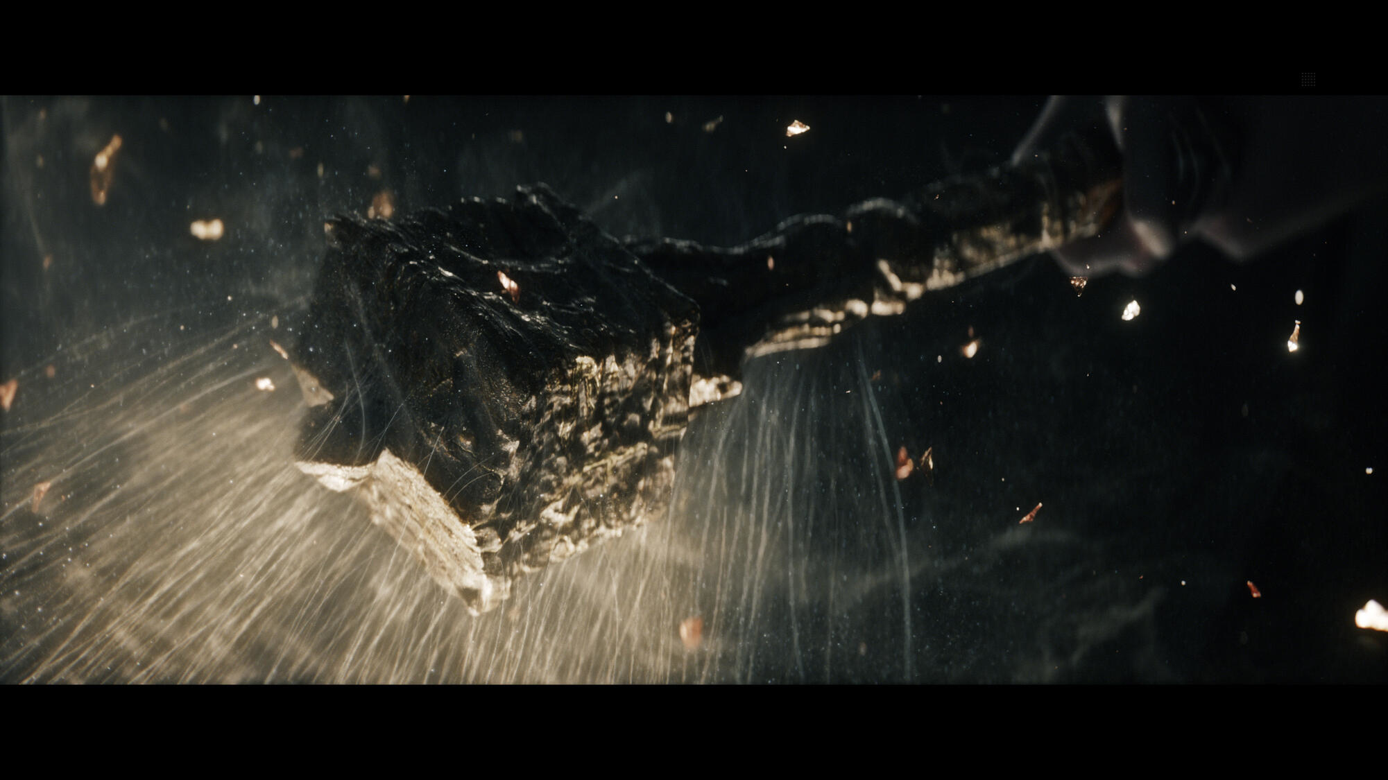 Drewniana broń trzymana w ciemnym otoczeniu, z unoszącymi się cząsteczkami. Dramatyczne i tajemnicze.