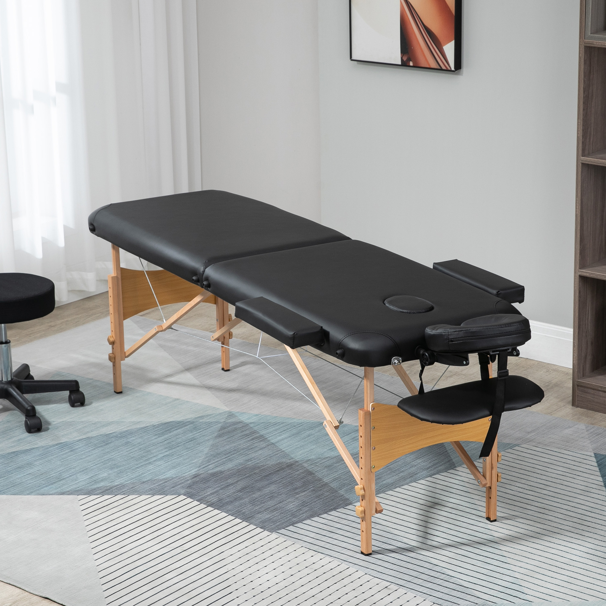 Una mesa de masaje en una habitación, con un taburete negro y una alfombra debajo.