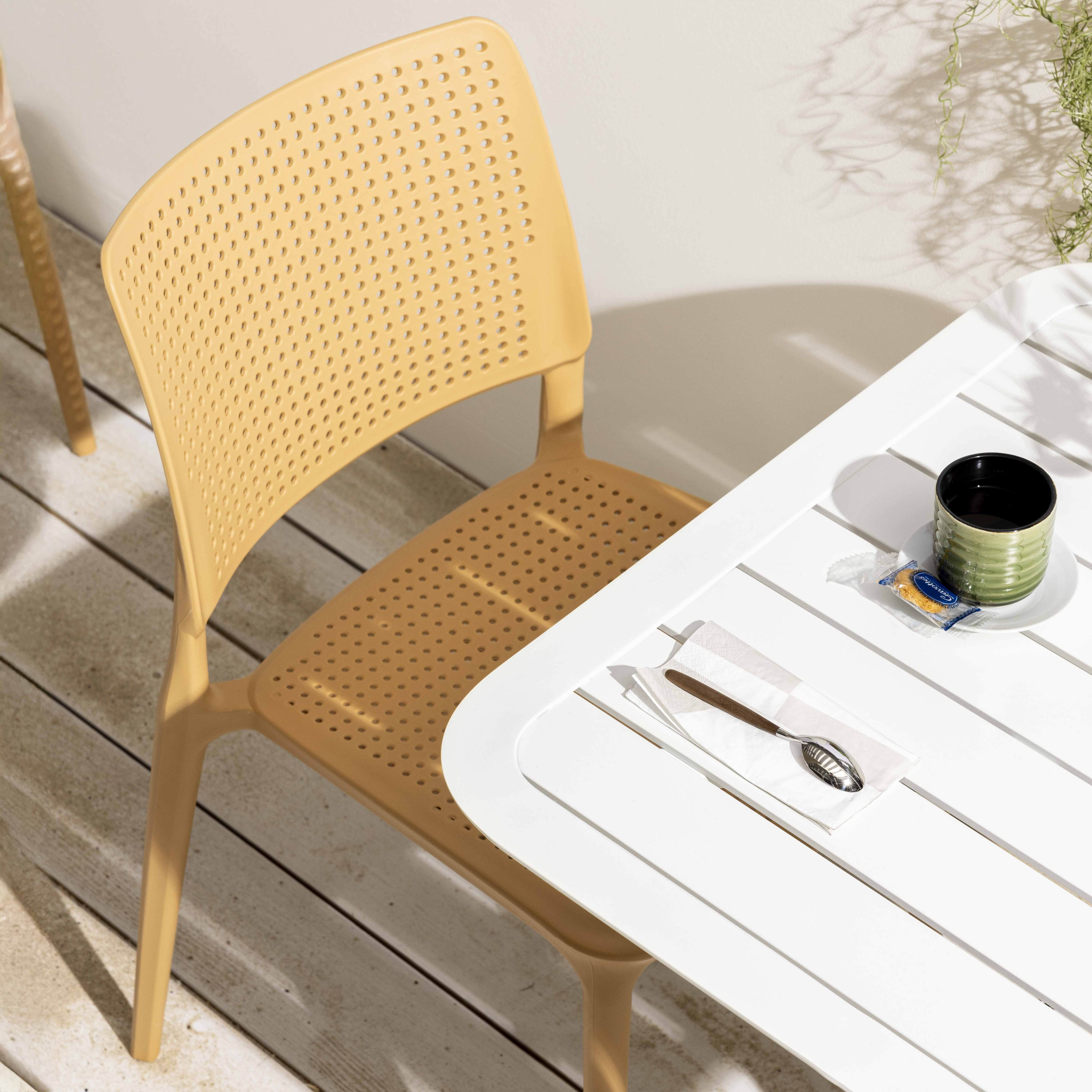 Hellbrauner perforierter Stuhl neben einem weißen Tisch mit Tasse und Serviette.