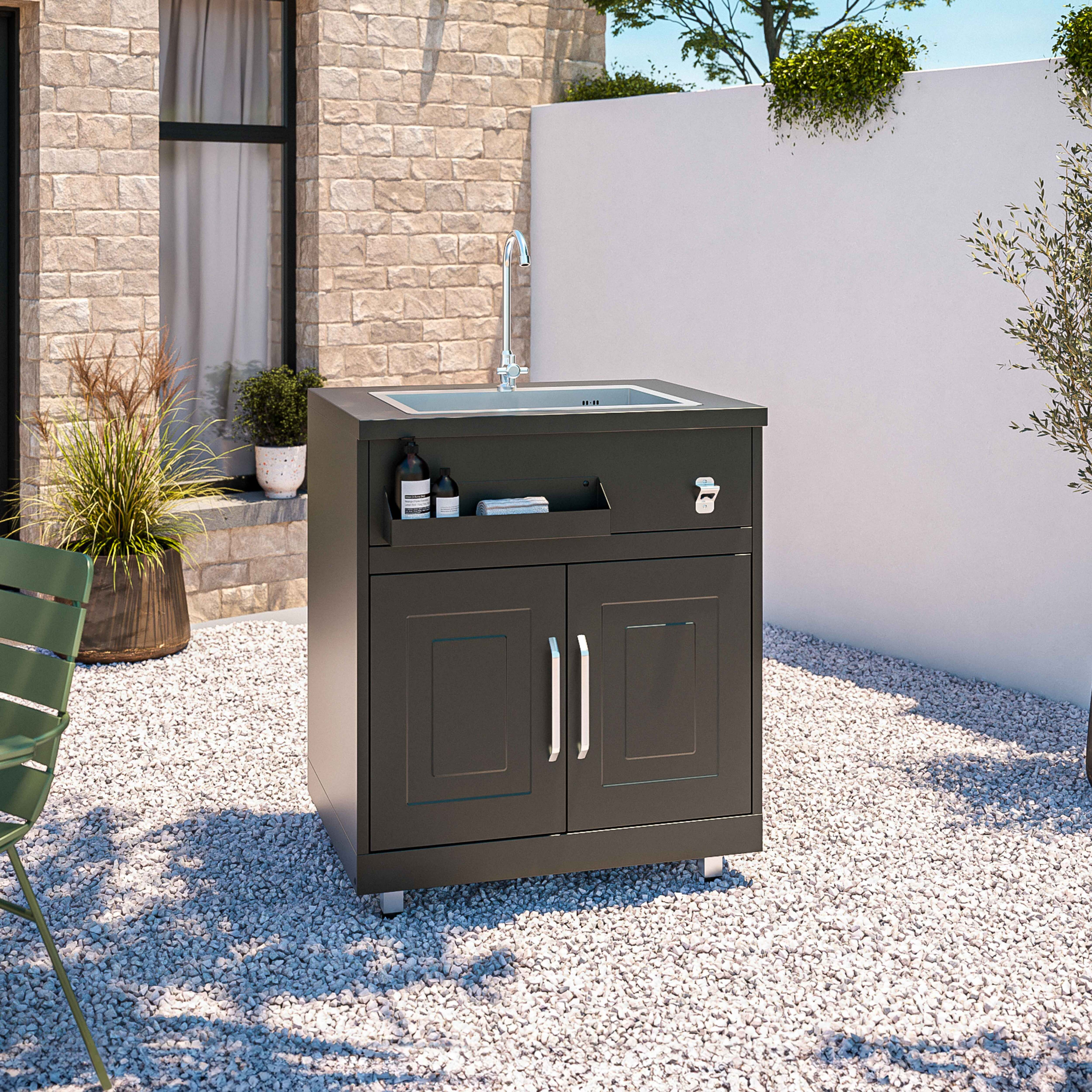 Dunkler Outdoor-Waschbeckenschrank mit Wasserhahn, umgeben von Kieselsteinen und einer Backsteinmauer.
