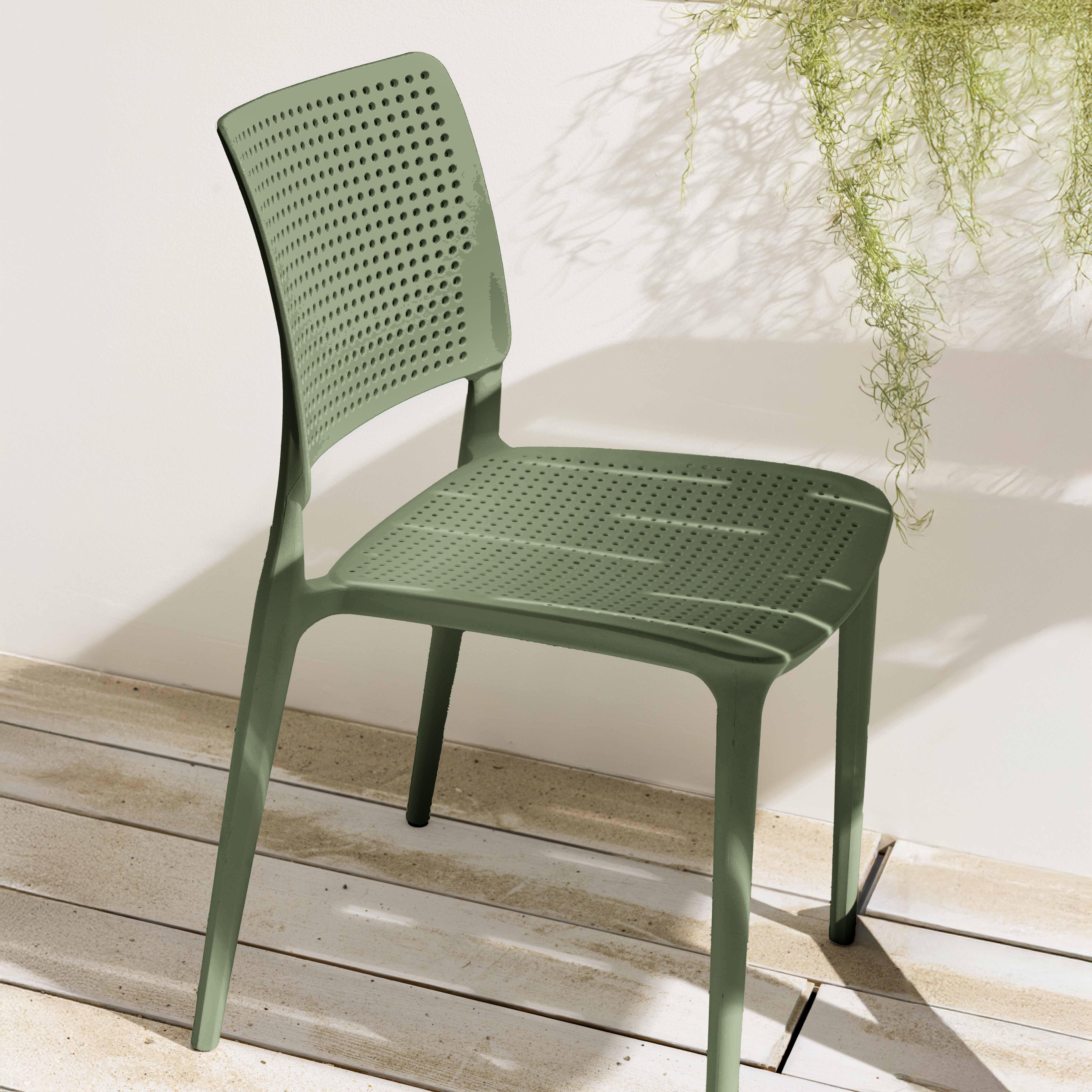 Grüner Kunststoffstuhl mit Löchern. Weißer Wandhintergrund, hängende Pflanze.