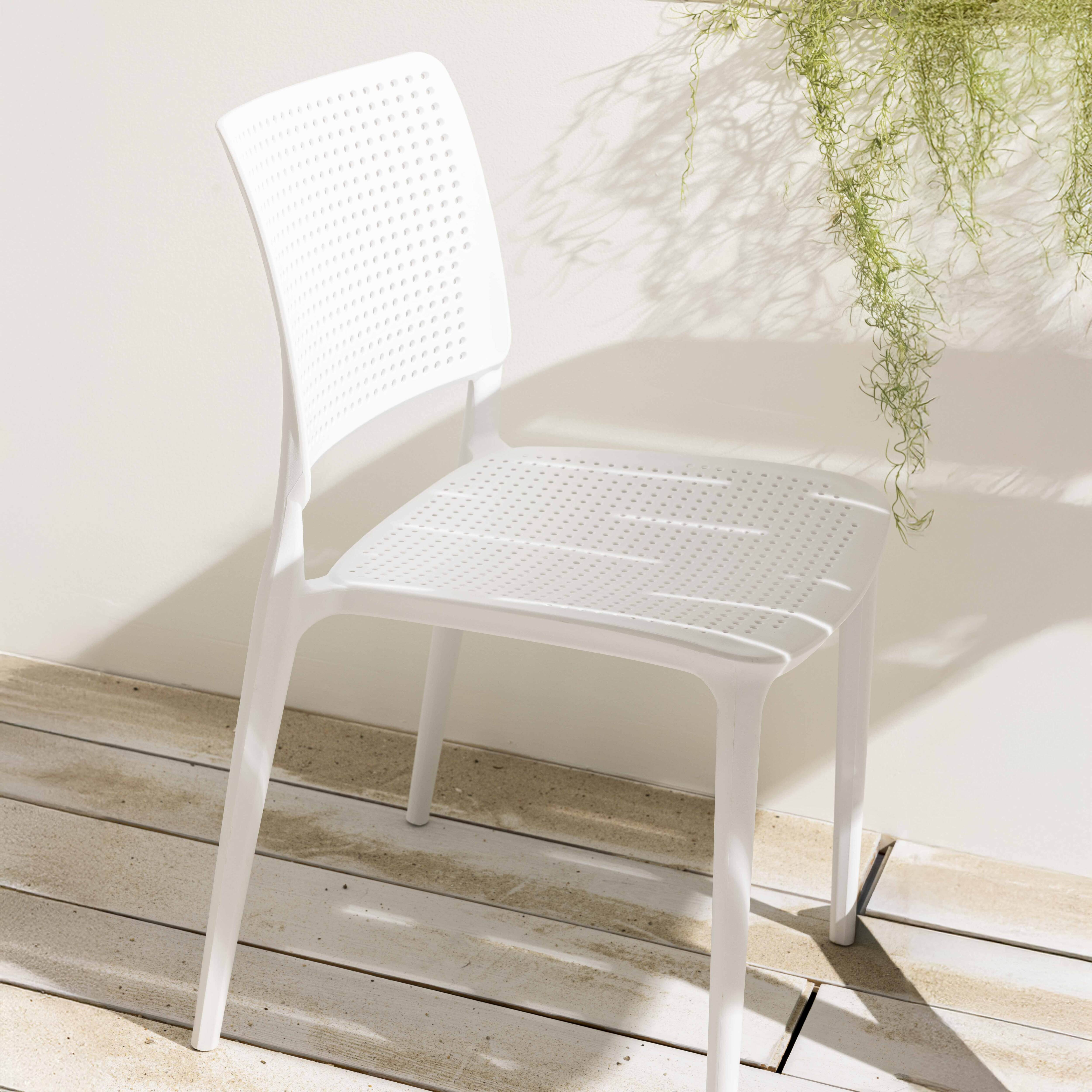 Weißer Kunststoffstuhl mit gelochtem Sitz und Rückenlehne. Pflanze im Hintergrund.