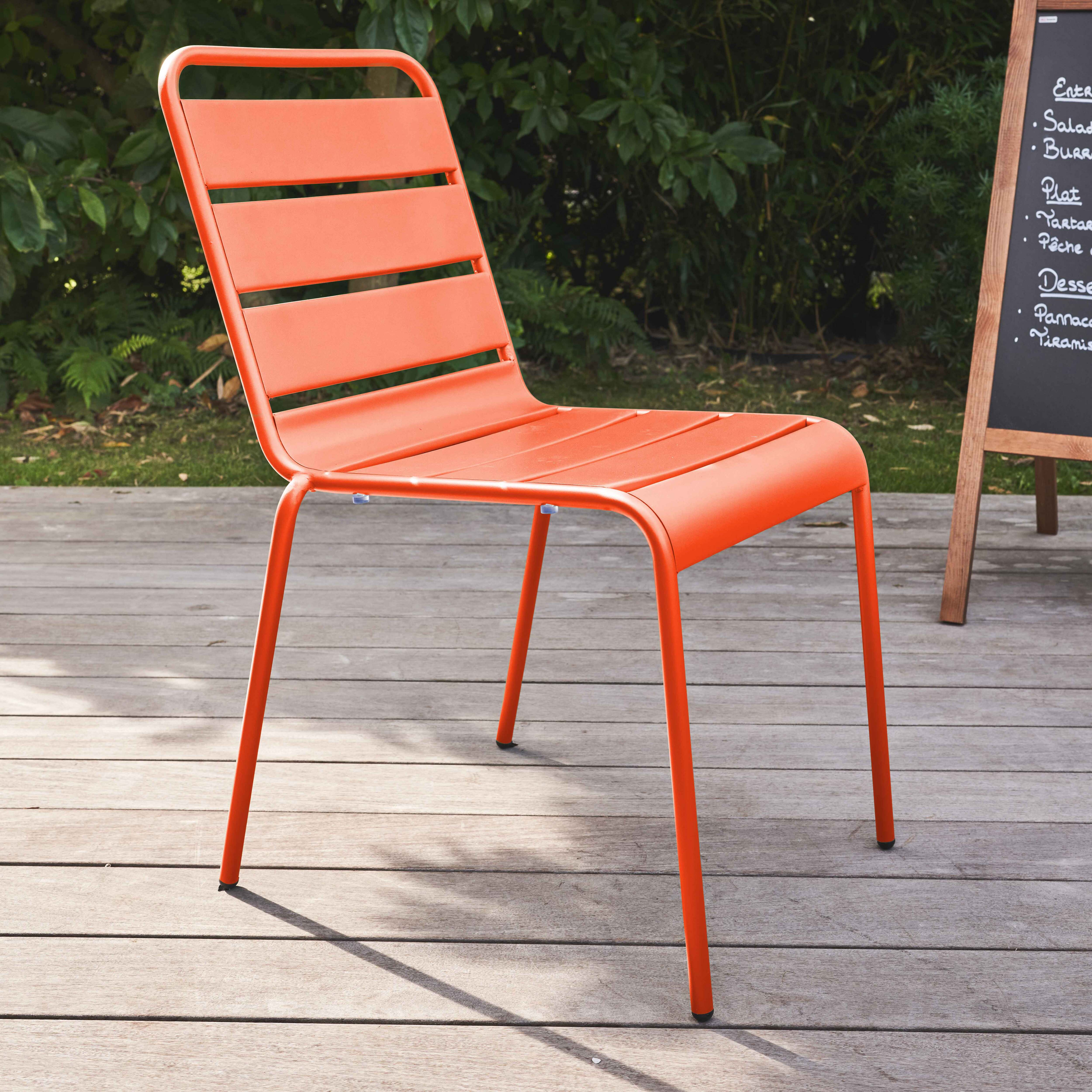 Orangener Stuhl auf Holzterrasse, mit verschwommenem Hintergrund, in der Nähe einer Tafel.