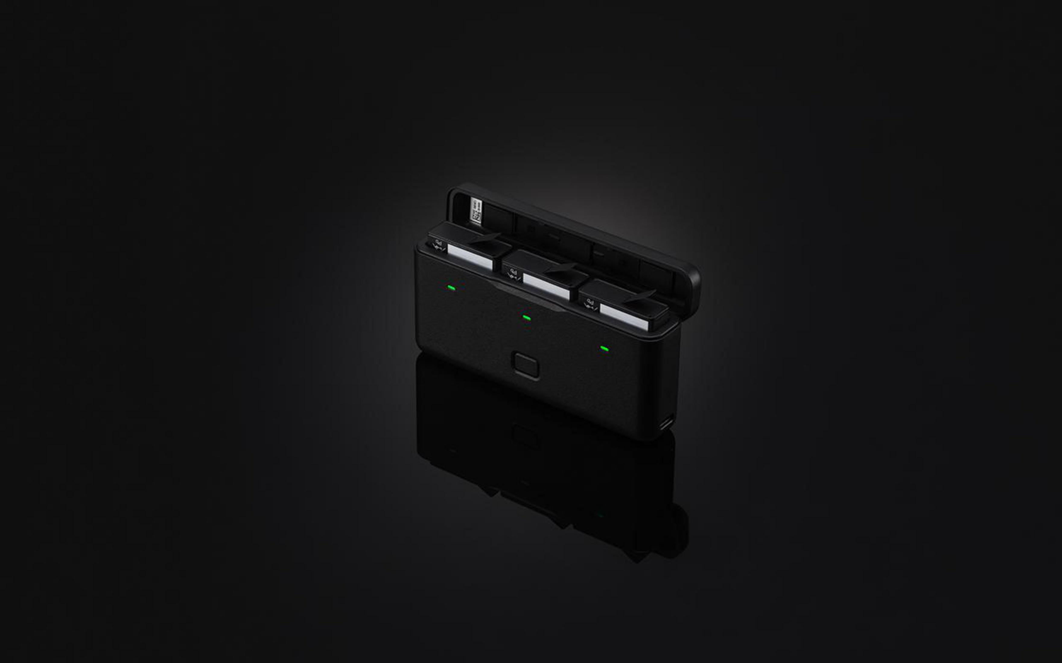 Czarna ładowarka z bateriami, otwarta. Ciemne tło.