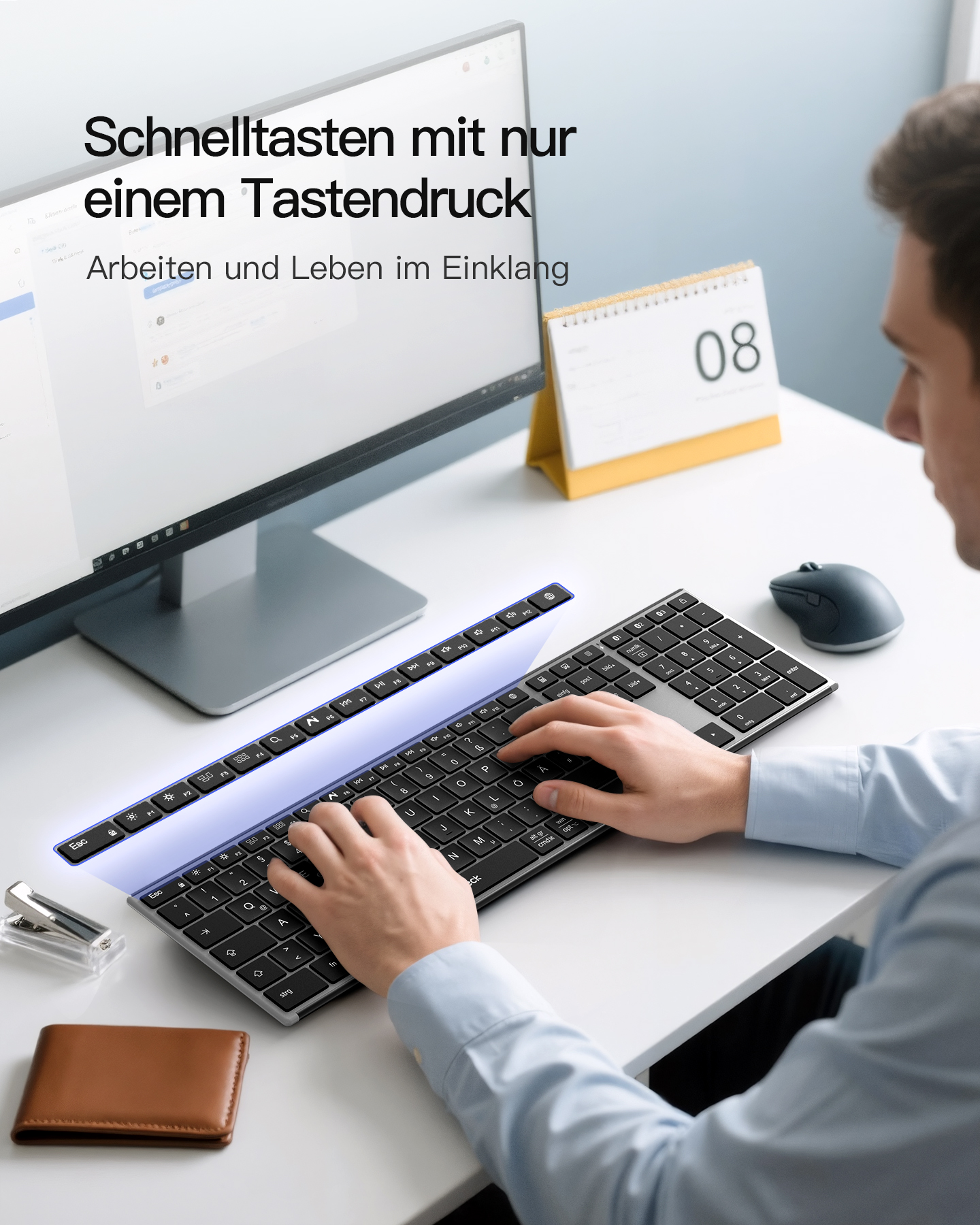 Ein Mann benutzt eine Tastatur und eine Maus an einem Schreibtisch mit einem Computermonitor, Kalender und Geldbörse.