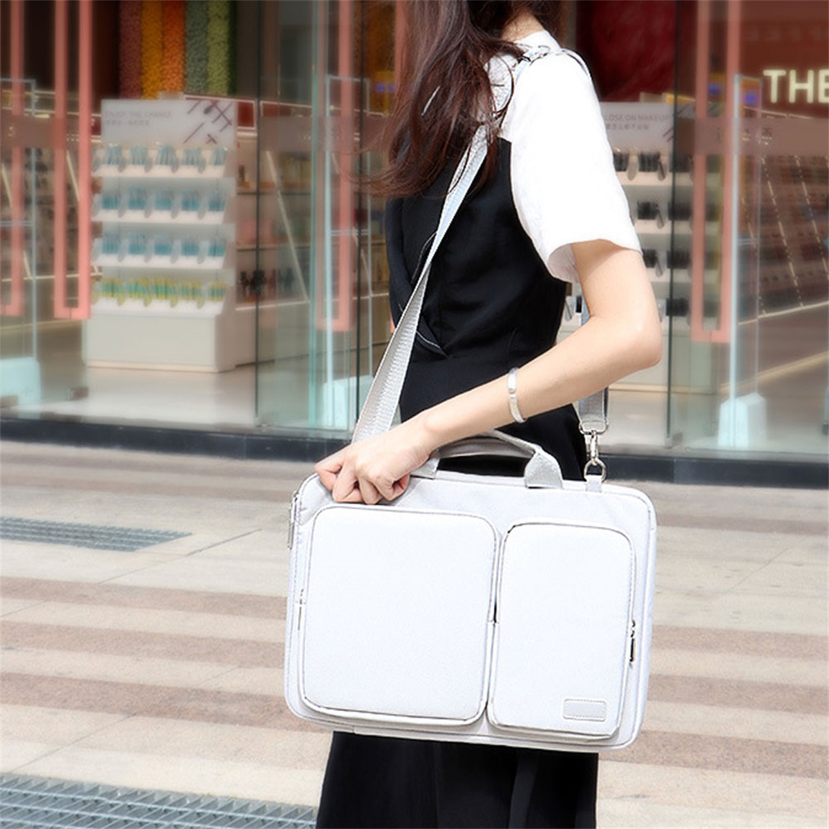 Frau, die eine hellgraue Umhängetasche mit zwei Vordertaschen trägt. Sie trägt ein dunkles Outfit.