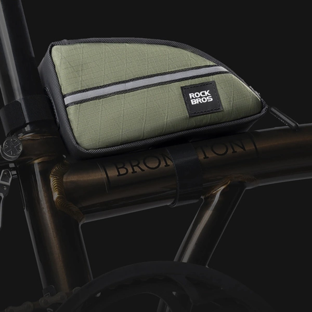 Grüne Fahrradtasche an einem braunen Fahrradrahmen befestigt, schwarzer Riemen und schwarzer Hintergrund.