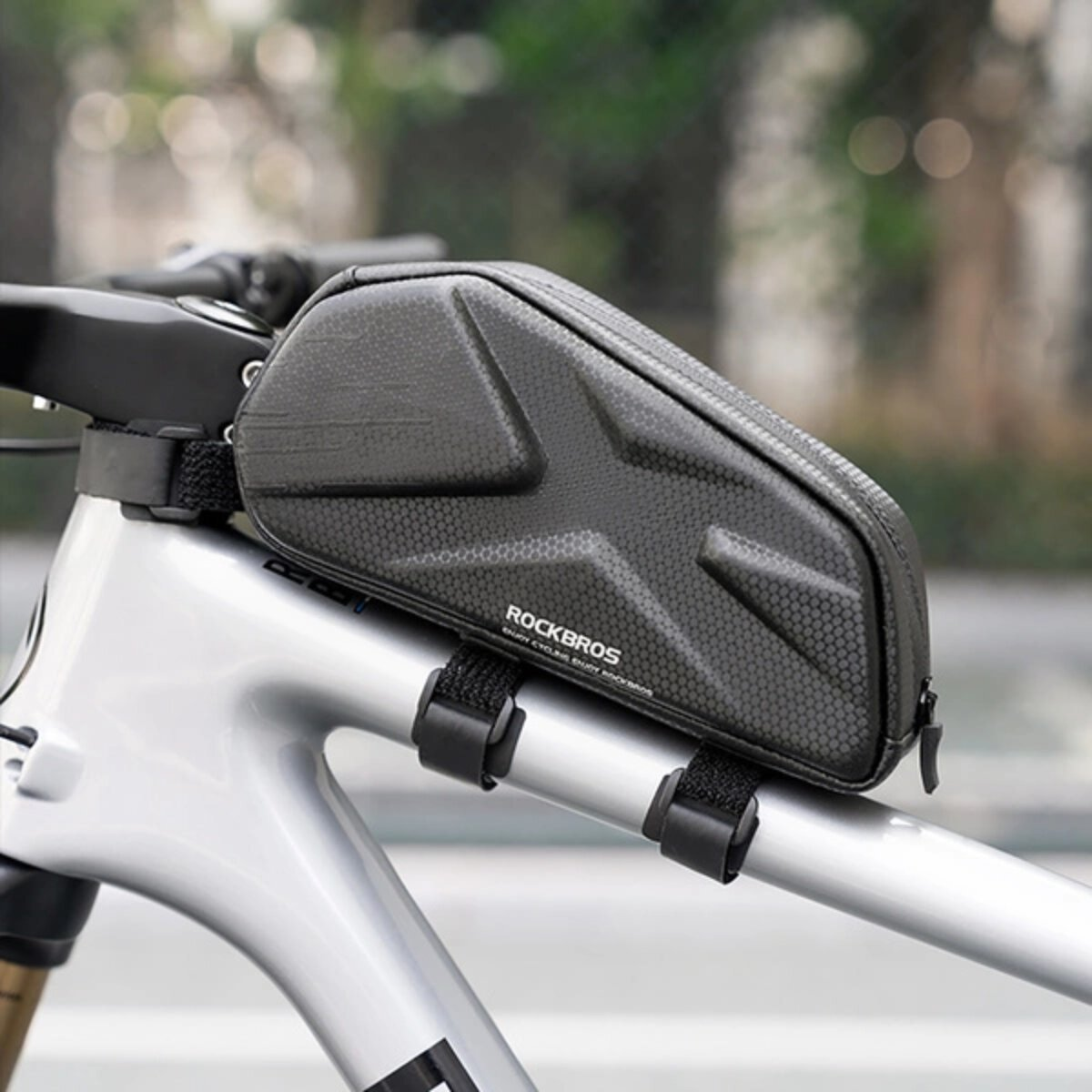 Schwarze Fahrradtasche an einem Fahrradrahmen befestigt, mit Wabenmuster, auf grauem Hintergrund.