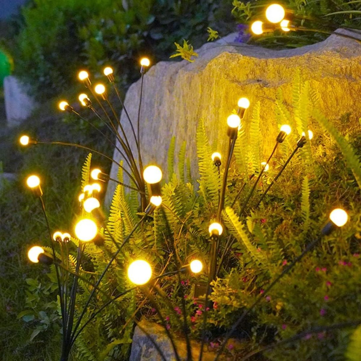 Mehrere Solar-Gartenleuchten mit weißen Glühbirnen in einem Garten mit grünen Pflanzen und einem Stein.