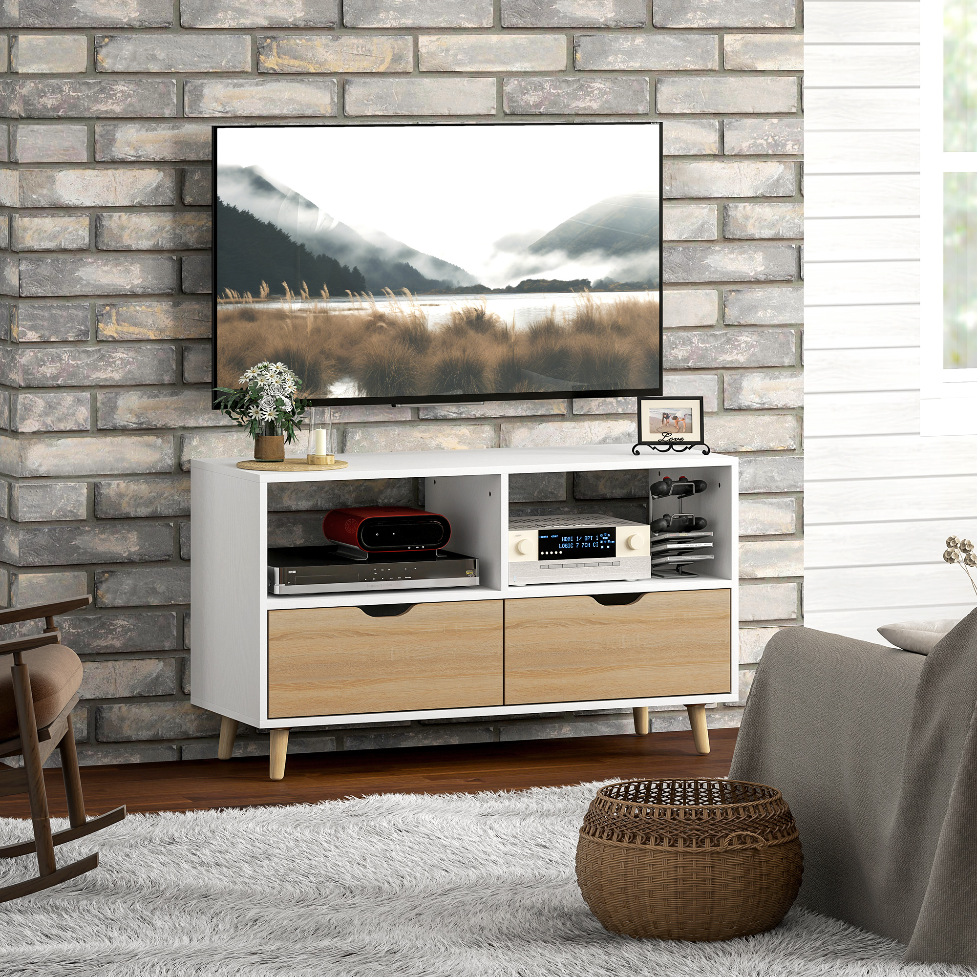 Weißer und Holz TV-Ständer mit TV, Bild und Deko vor einer Backsteinmauer.