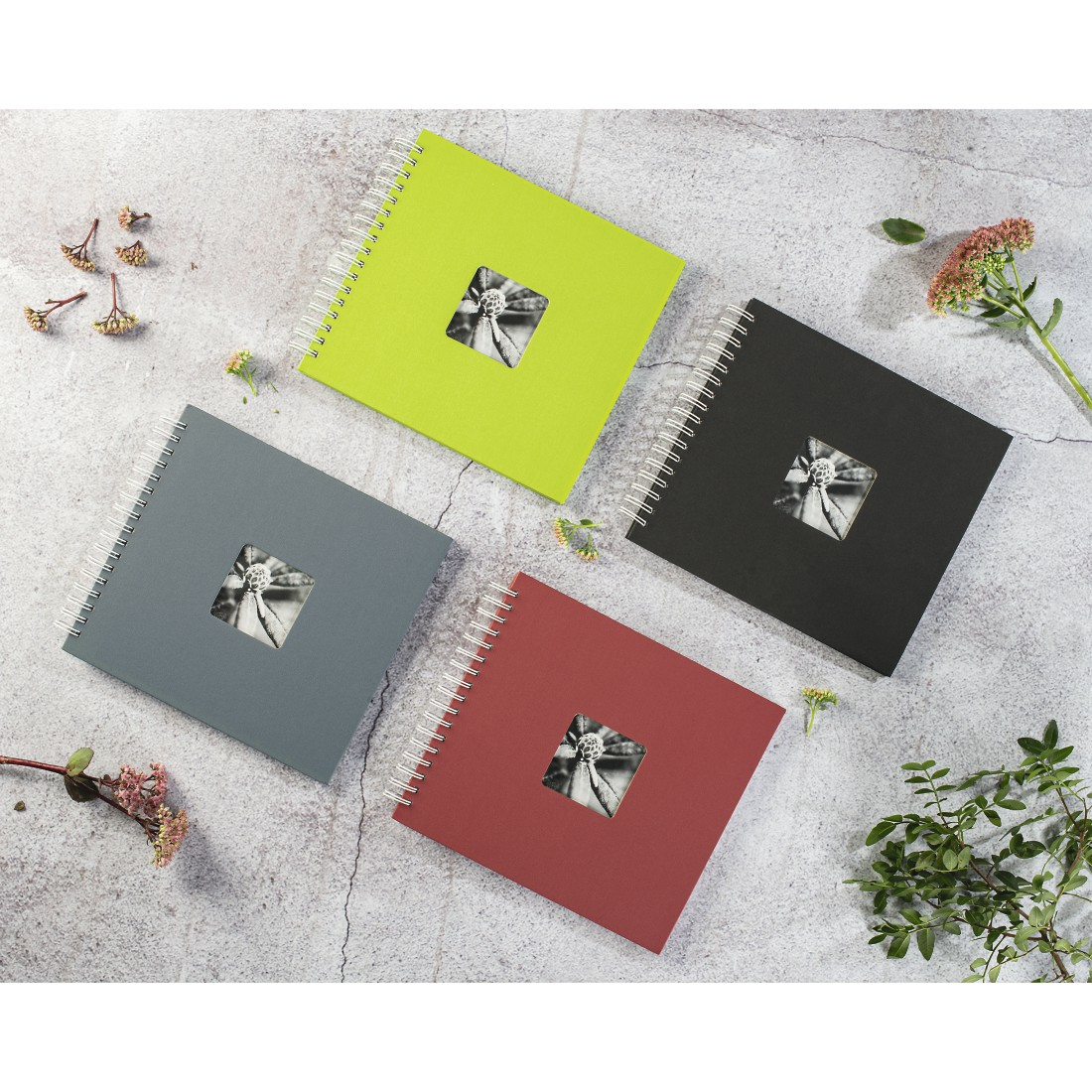 Cztery albumy fotograficzne z kwadratowym wycięciem, ułożone na teksturowanej powierzchni.