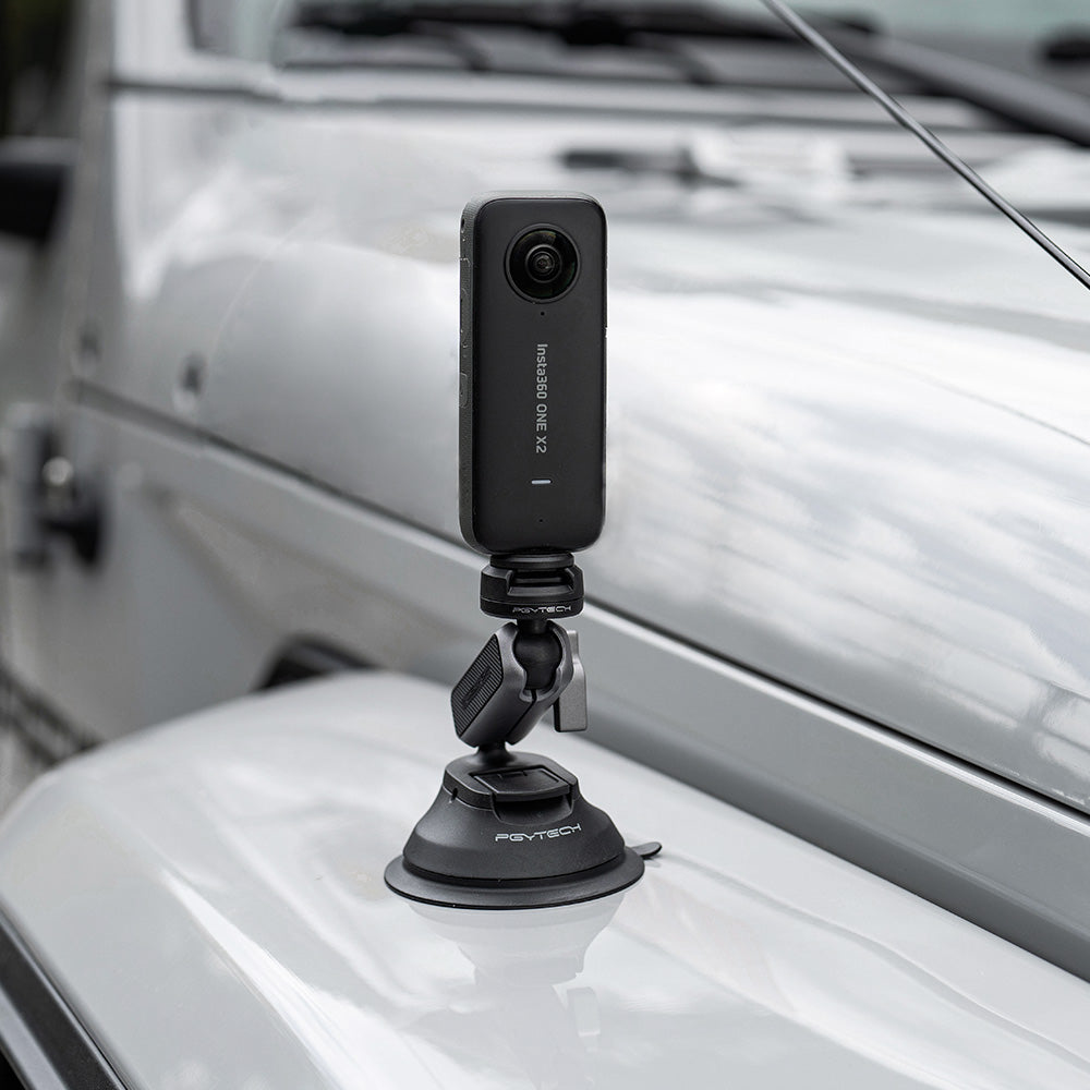 Schwarze Insta360-Kamera mit Saugnapf auf Motorhaube, nach vorne gerichtet.