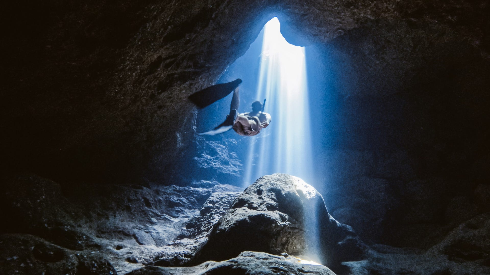 Nurek pływa w jaskini, a światło słoneczne wpada przez otwór.