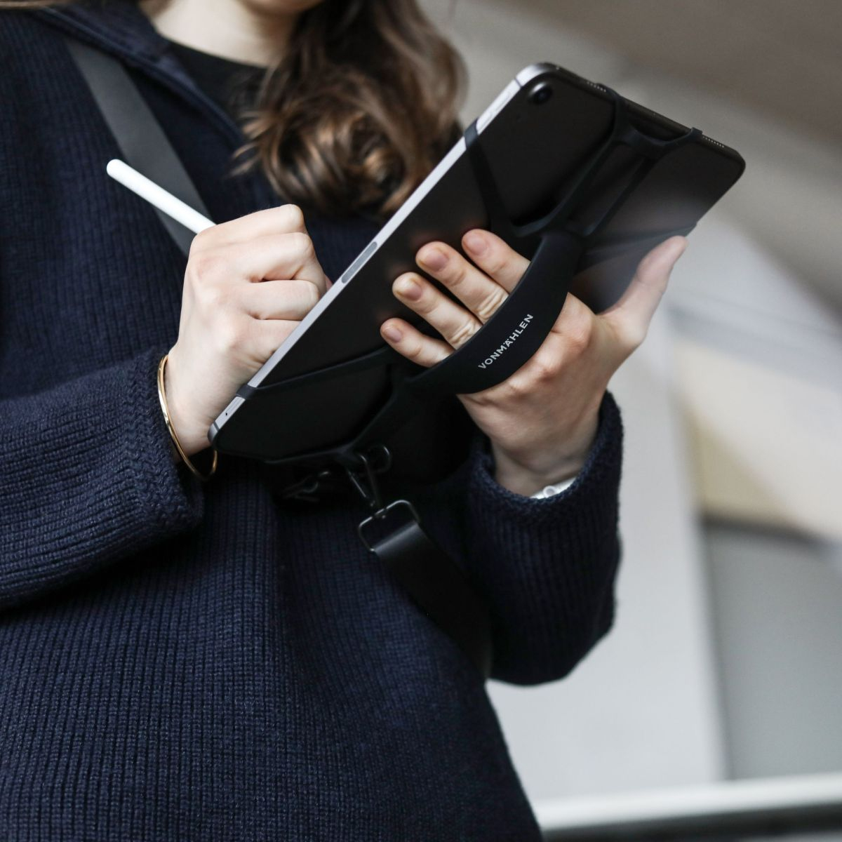Eine Person hält ein Tablet mit schwarzem Riemen, in der Nähe eines weißen Stifts.