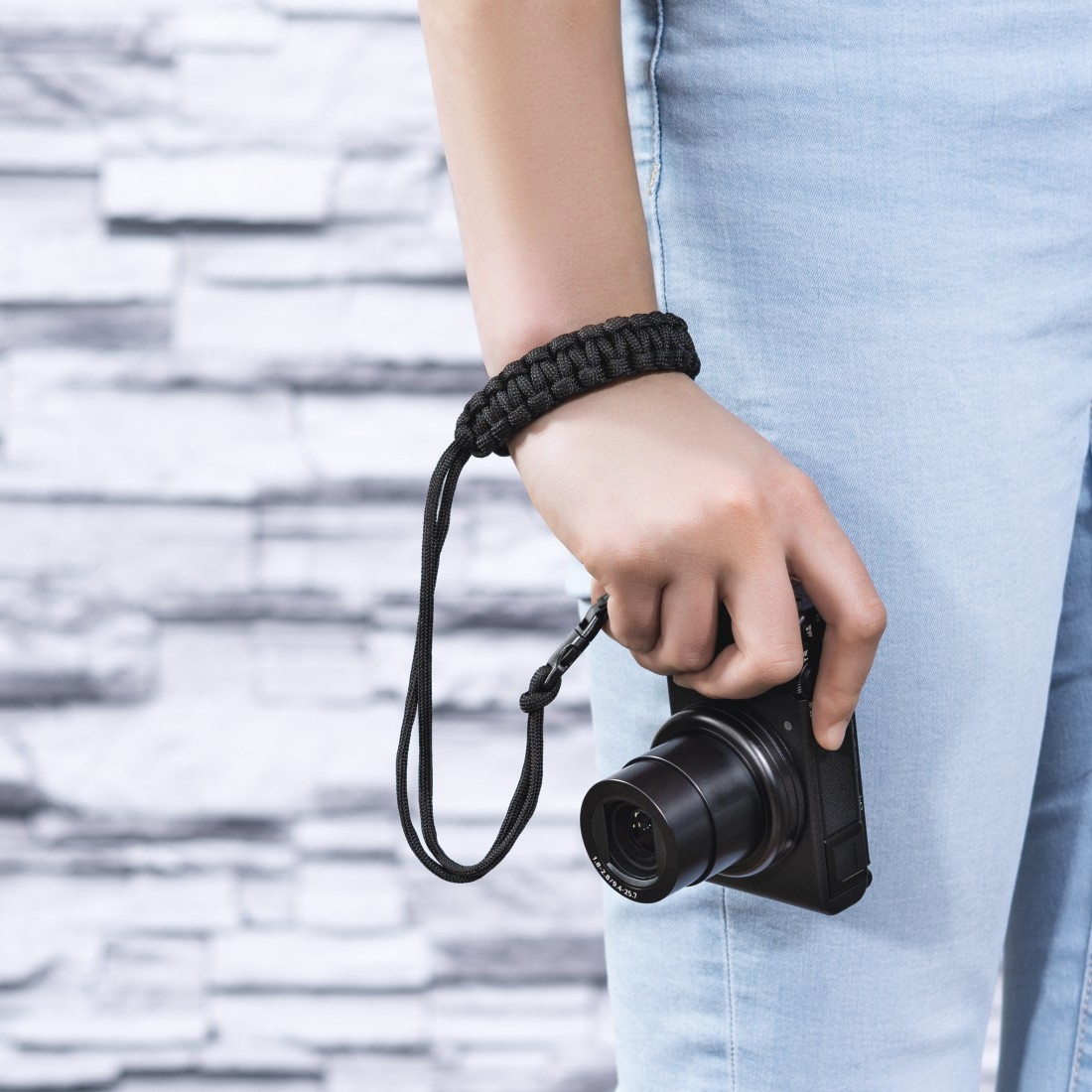 Osoba trzymająca czarny aparat z czarnym paskiem na nadgarstek i czarną plecioną bransoletką.