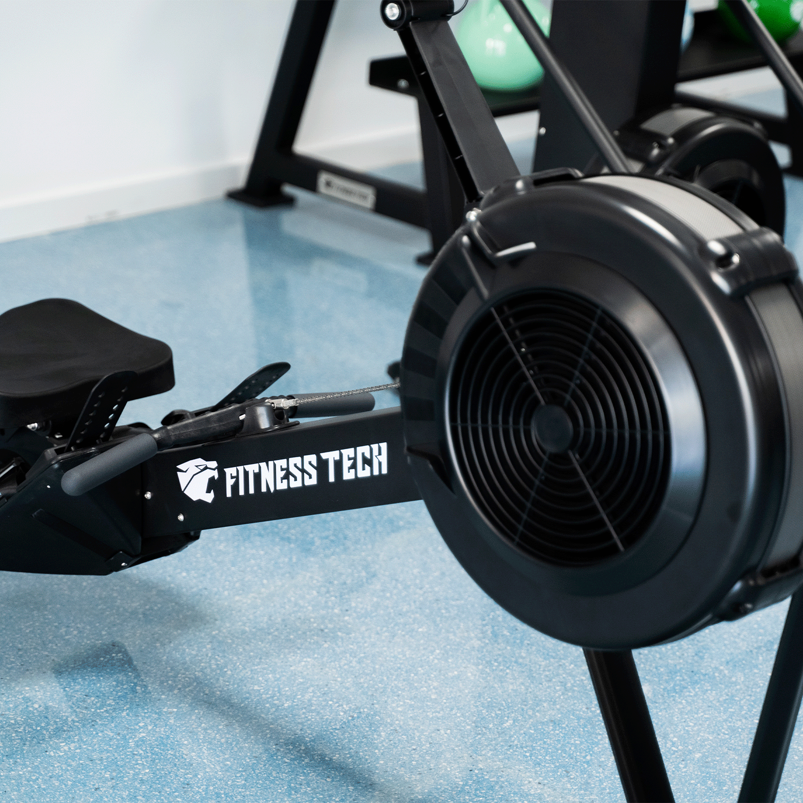 Macchina per il canottaggio nera con logo Fitness Tech su pavimento blu in palestra.