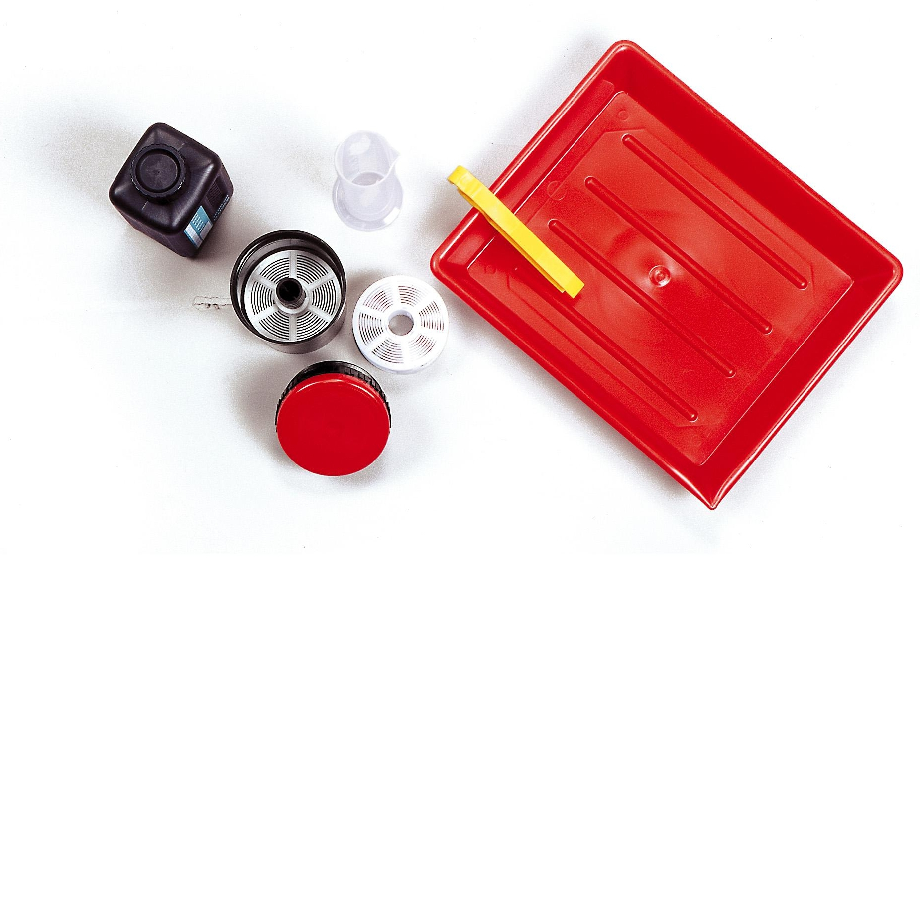 Zestaw do wywoływania zdjęć. Czarny pojemnik, czerwona tacka, rolki filmu. Białe tło.