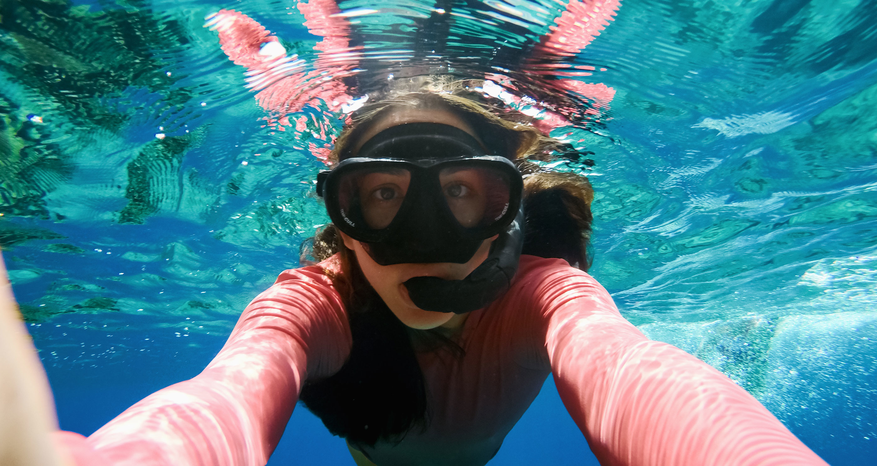 Donna con attrezzatura da snorkeling sott'acqua, guarda la fotocamera. Acqua blu.