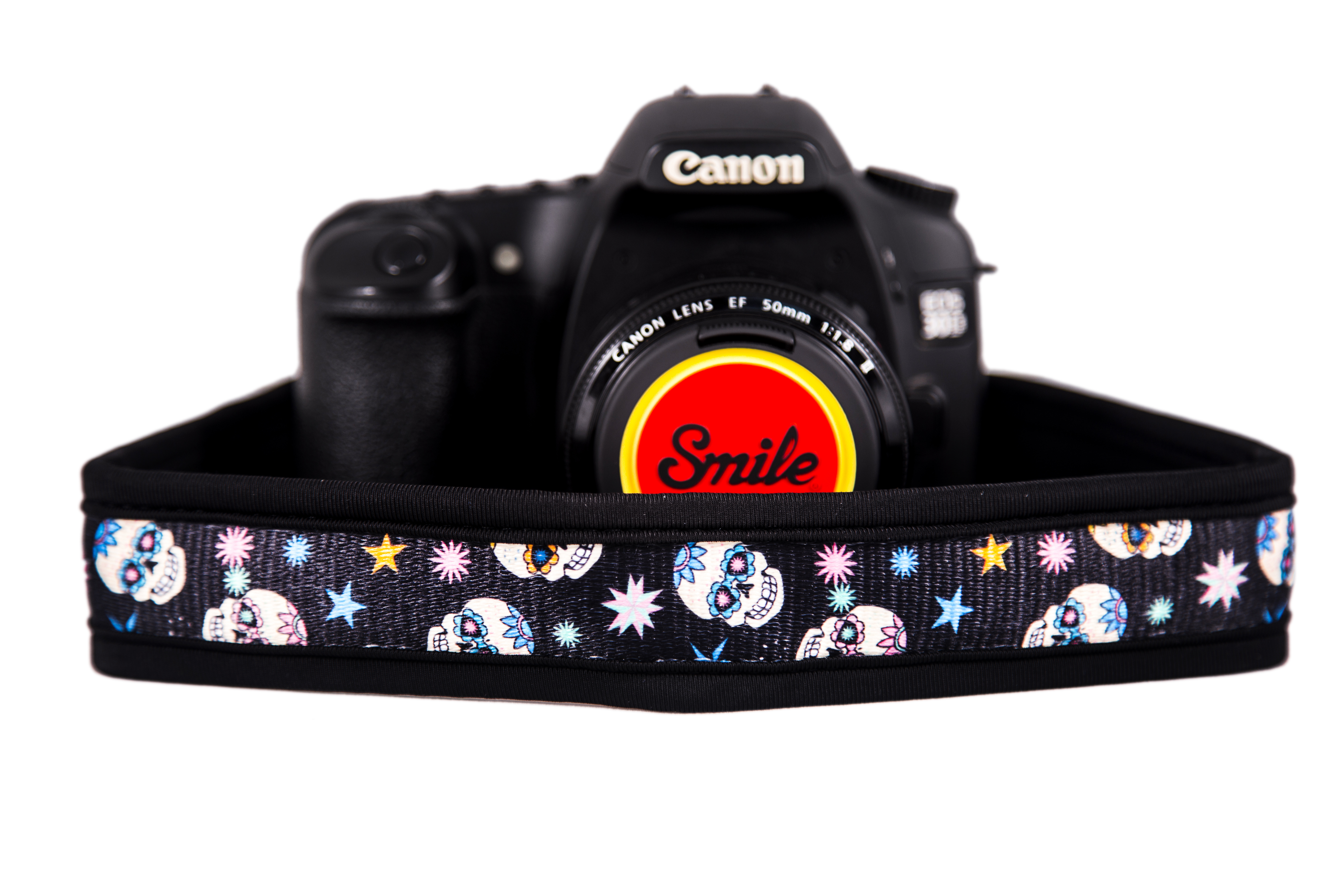 Una cámara negra con una correa colorida con calaveras y estrellas, y una tapa de lente roja.