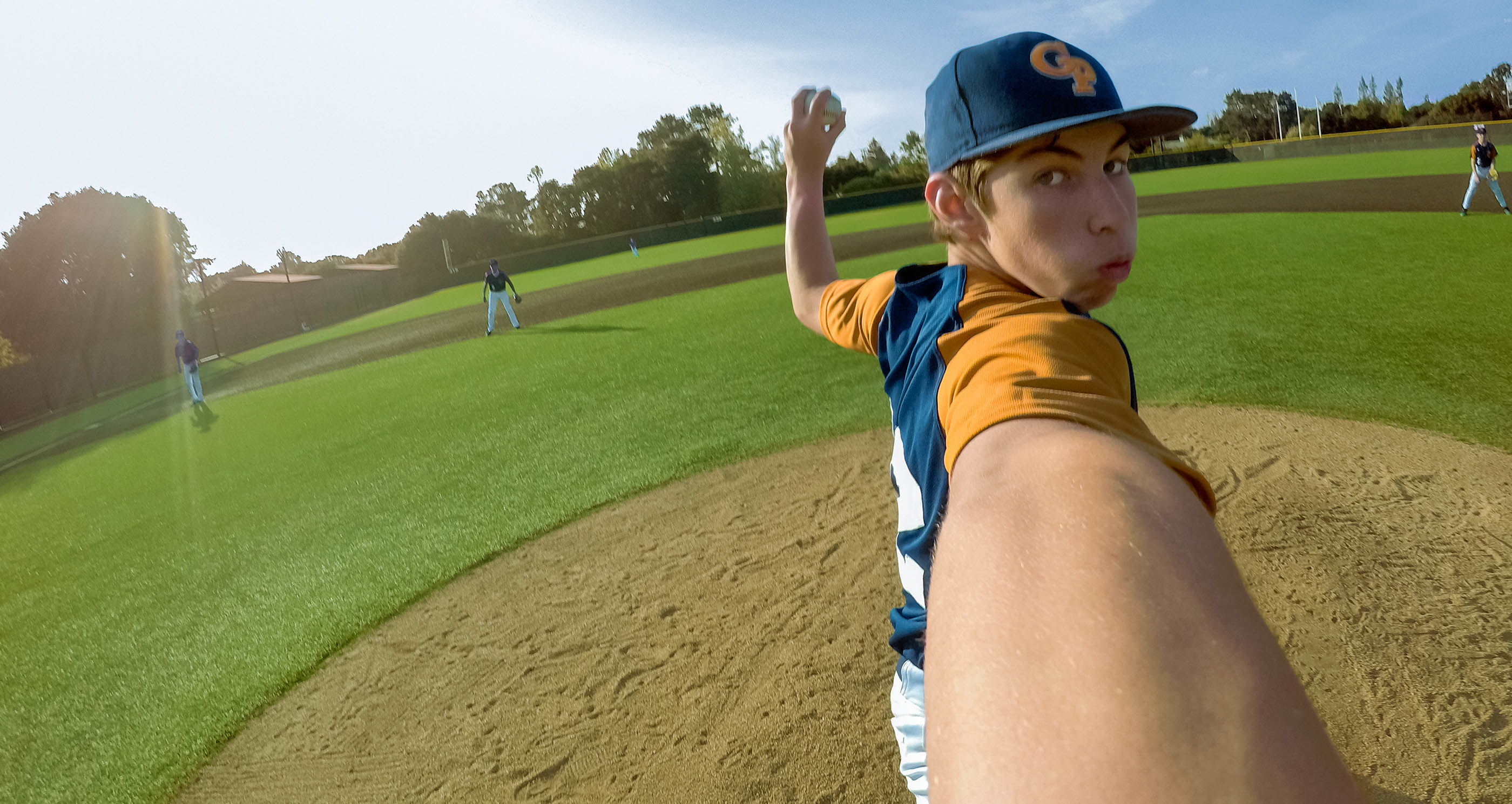 Chłopiec rzuca piłkę bejsbolową na boisku. W tle inni gracze.