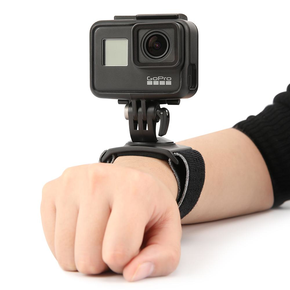 Kamera GoPro zamontowana na pasku na nadgarstek. Ręka trzyma kamerę, skierowaną do przodu.