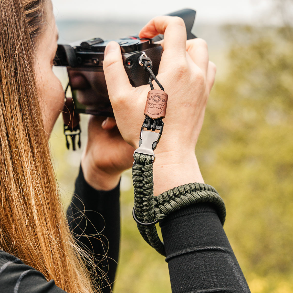 Una persona che tiene una fotocamera con una tracolla verde. La tracolla è intorno al polso.