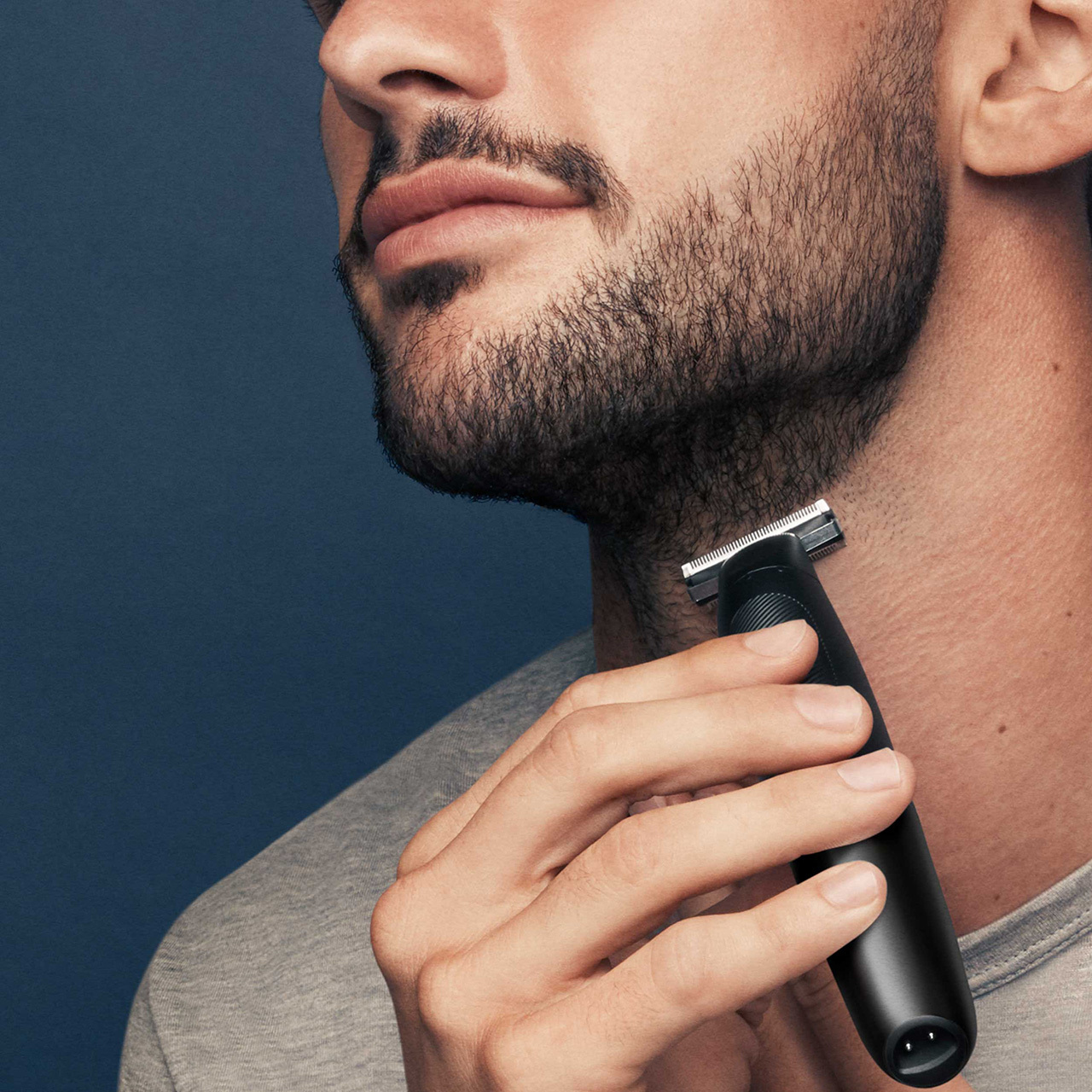 Man trimming his neck with a trimmer, close-up, dark background.