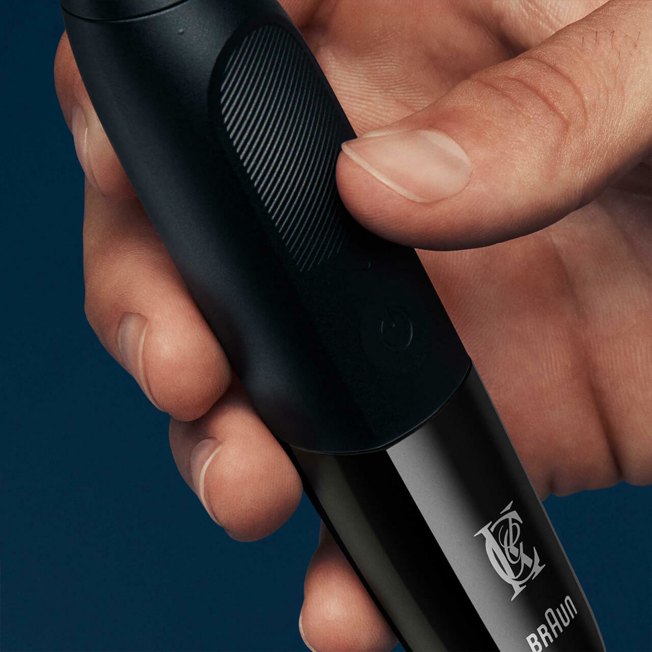 Hand holding a black Braun trimmer, close-up, dark blue background.