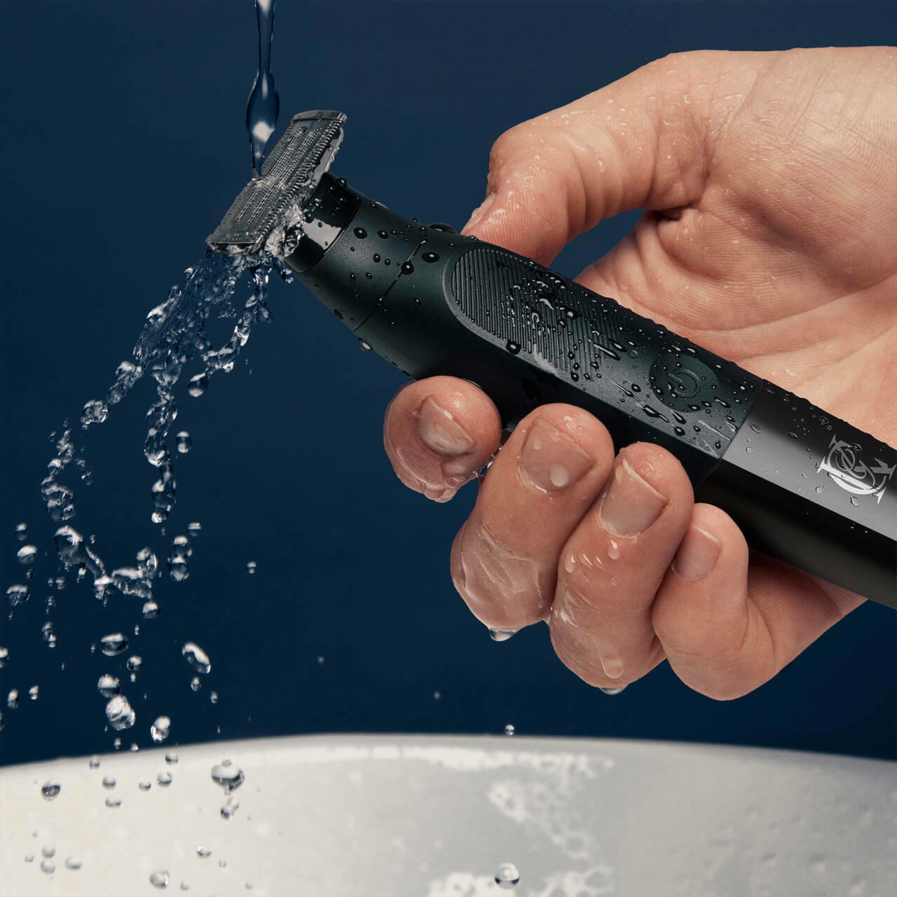 Man's hand holding a trimmer, water splashing, blue background.