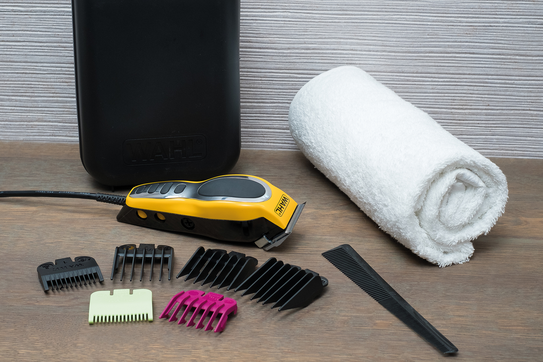 Haarschneider-Set mit Zubehör, Handtuch und Koffer auf Holzoberfläche.