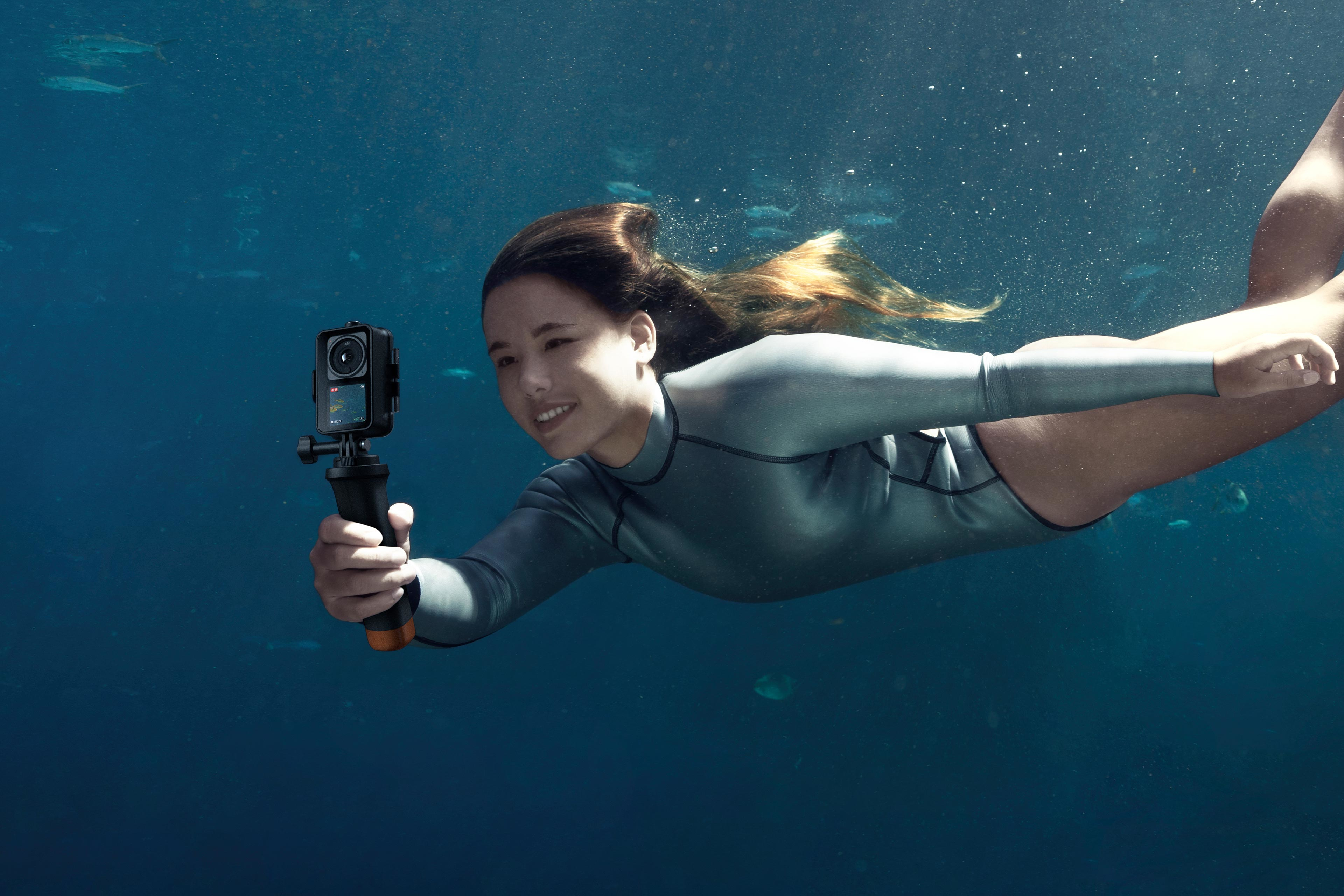 Kobieta w wodzie trzymająca aparat. Uśmiecha się i patrzy w kamerę.